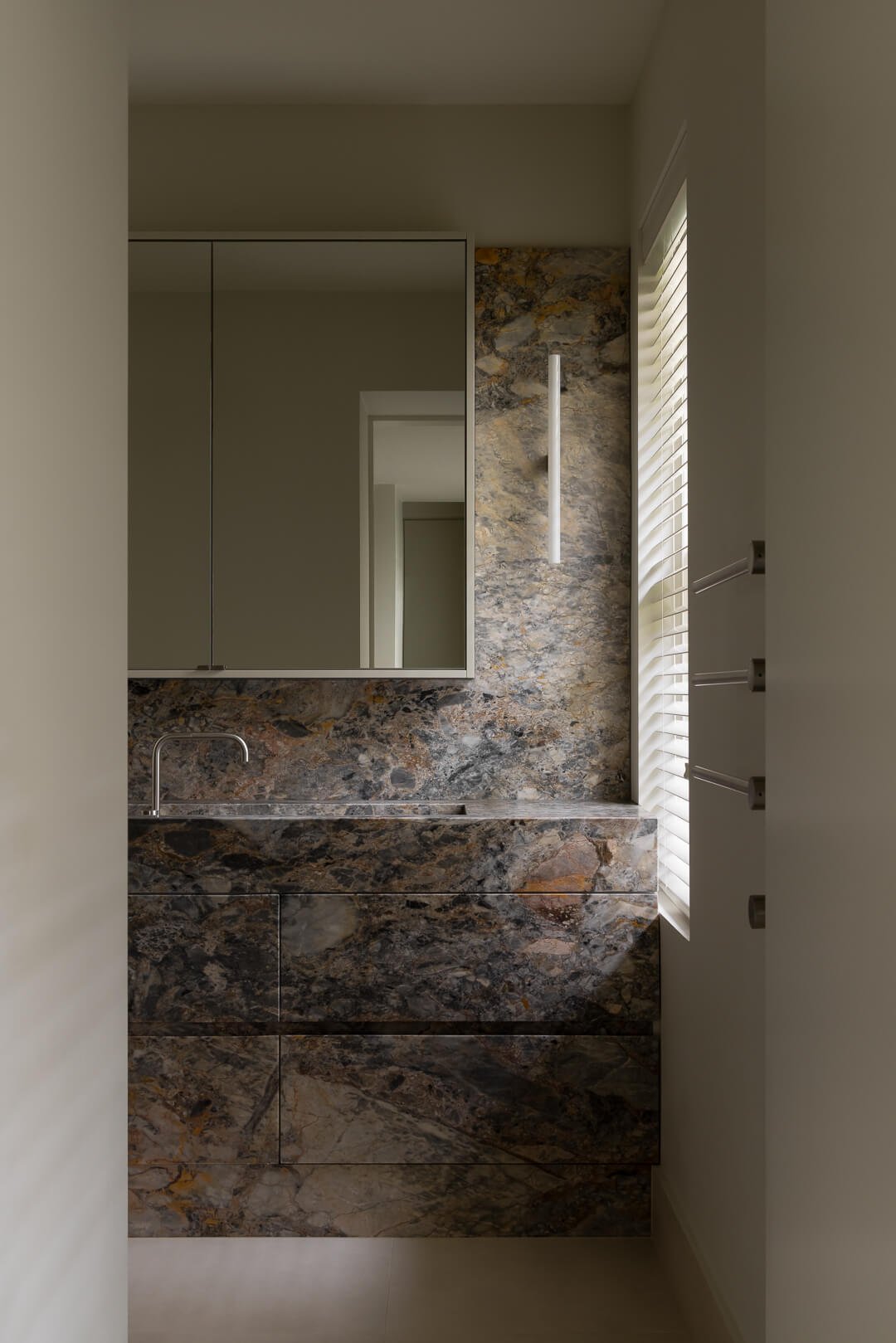 Modern luxury bathroom with custom natural stone vanity, integrated sink, and vertical wall sconce at Silver House.