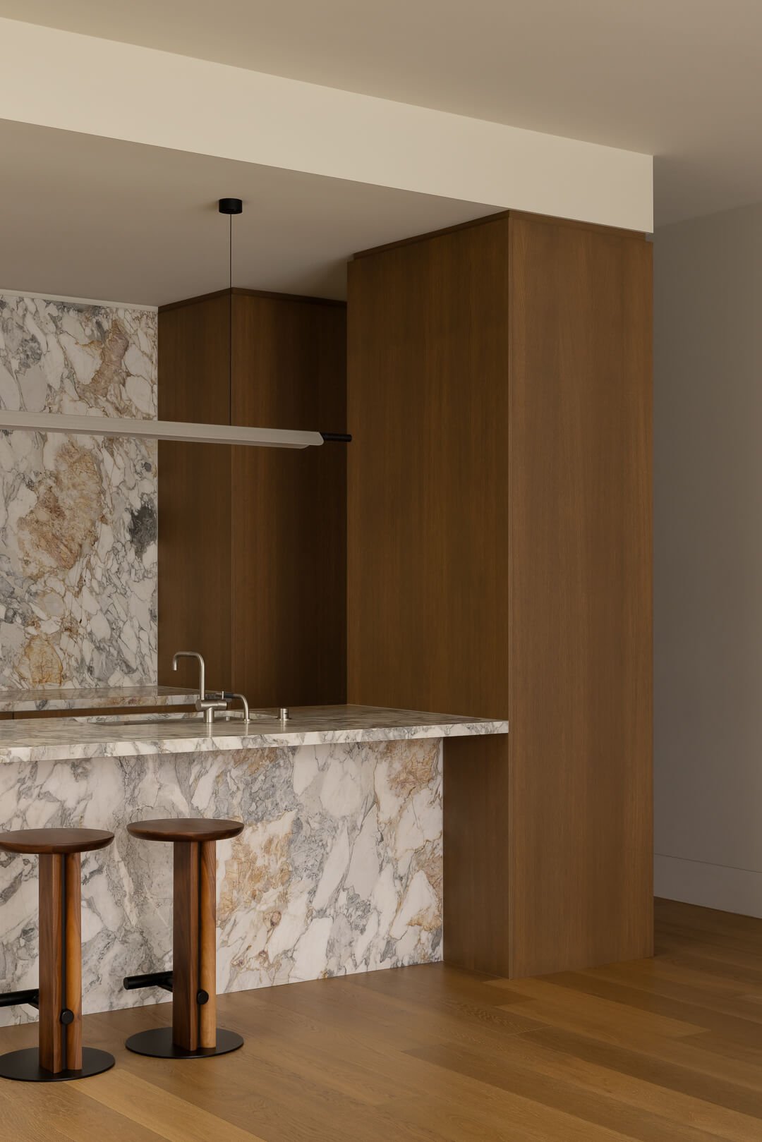 Close-up of a Kalana natural stone kitchen island with a Vola brushed nickel mixer and timber bar stools at Silver House.