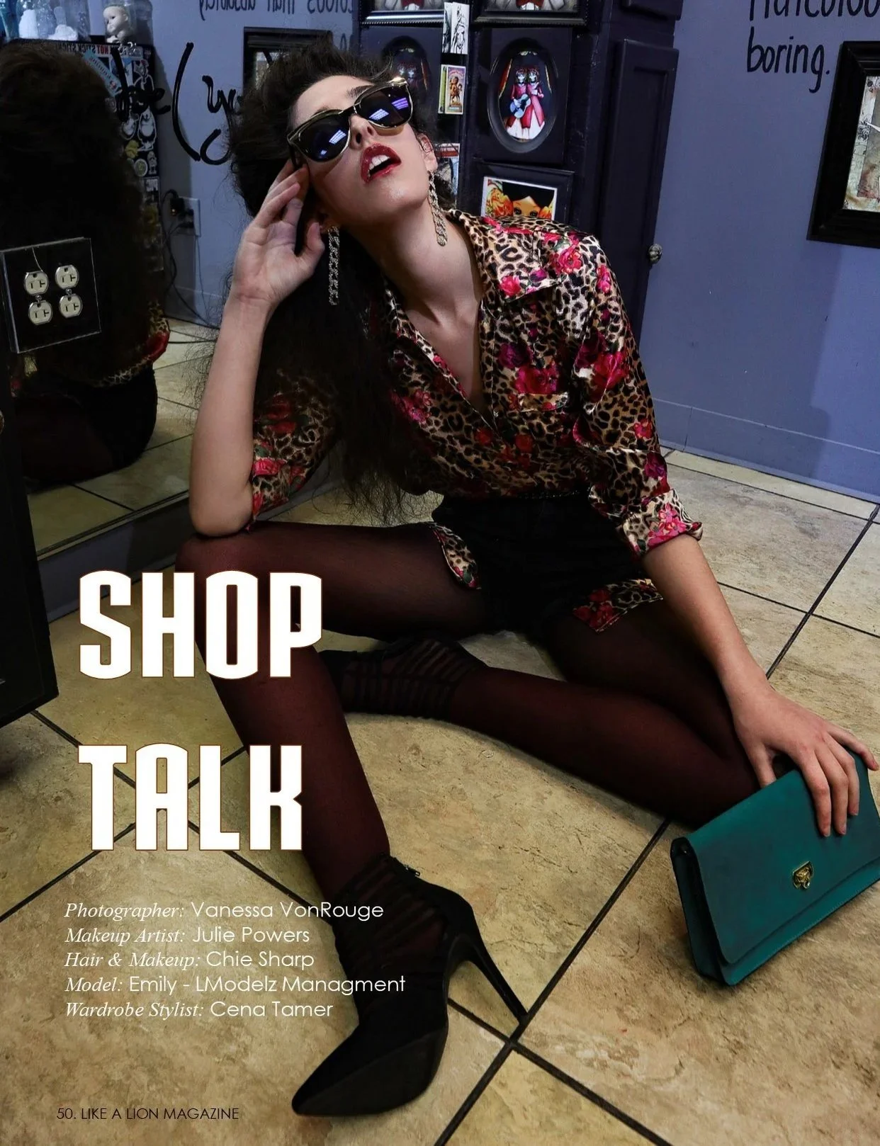 A woman wearing sunglasses, a leopard print shirt with pink flowers, and dark tights, is sitting on the floor with her legs spread apart, holding a teal clutch. She is in a store or gallery with framed pictures on a wall behind her. Text on the image