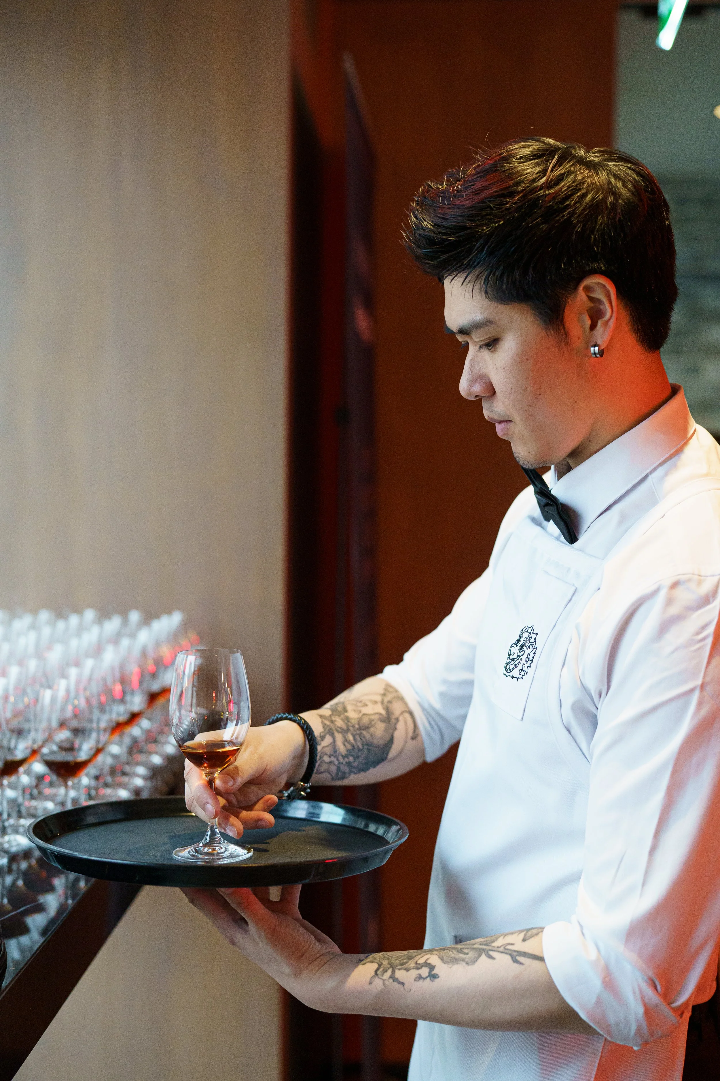 A server in white adding wine glasses to a tray.