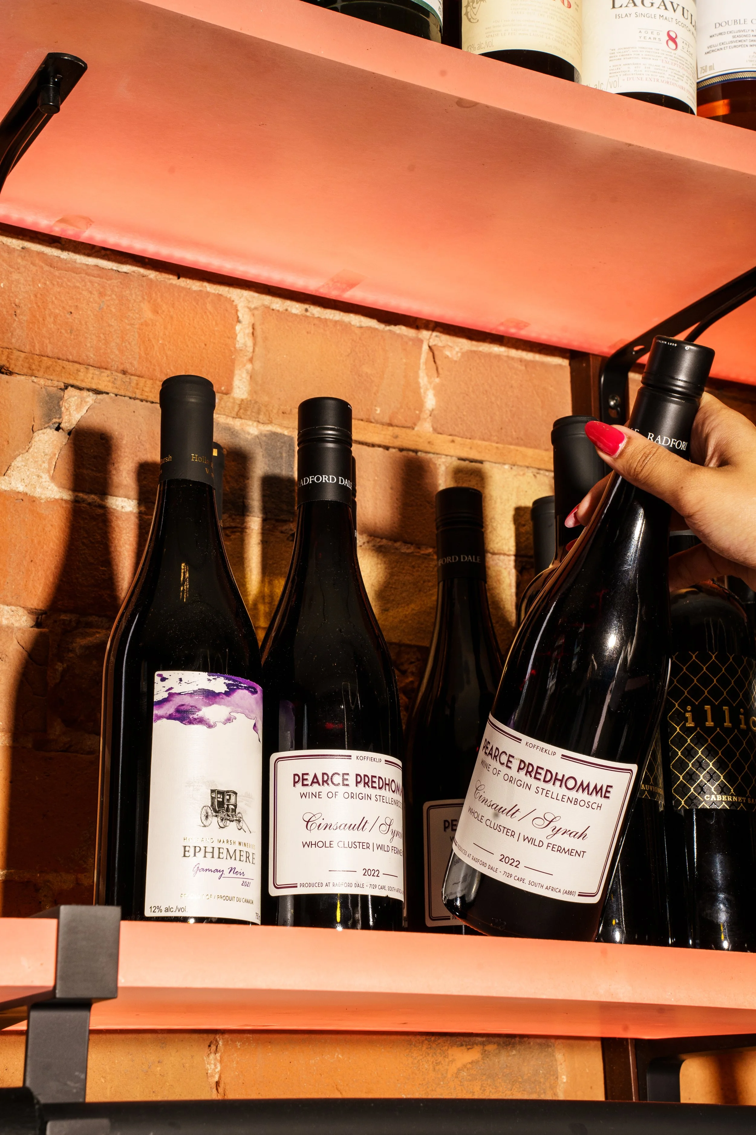 A hand reaching for a bottle of wine from a shelf full.