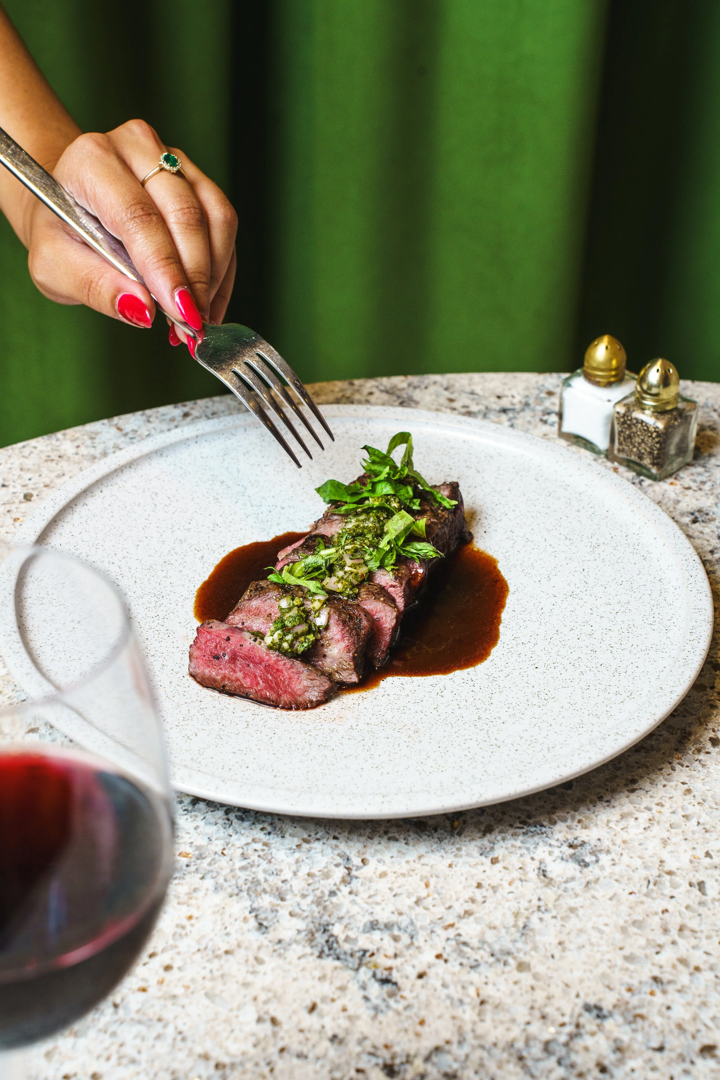 A styled plate of dinner, with a manicured hand reaching in with a fork to eat it.