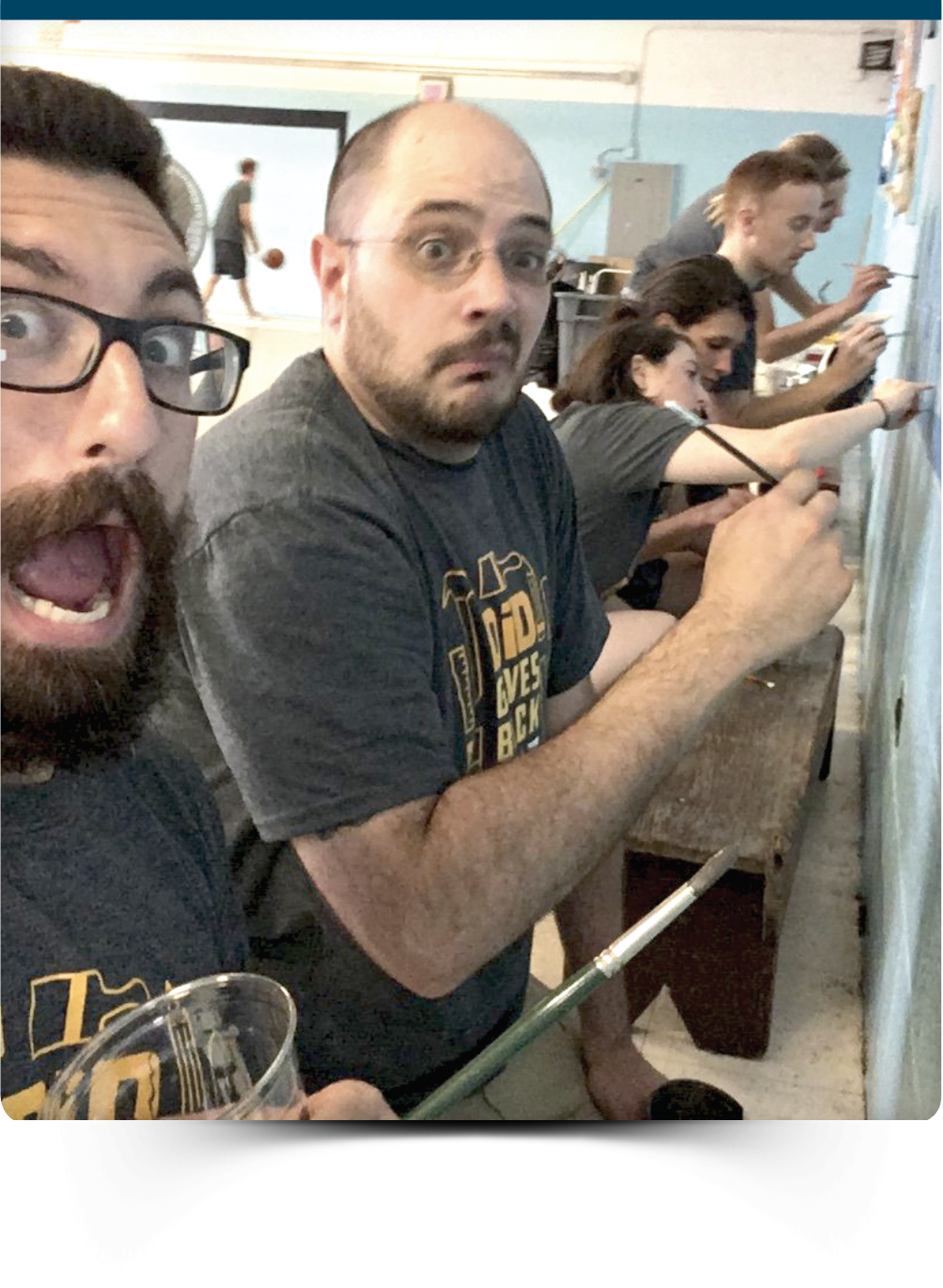 Group of people in a room painting a wall, one person in foreground with surprised facial expression, others focused on painting.