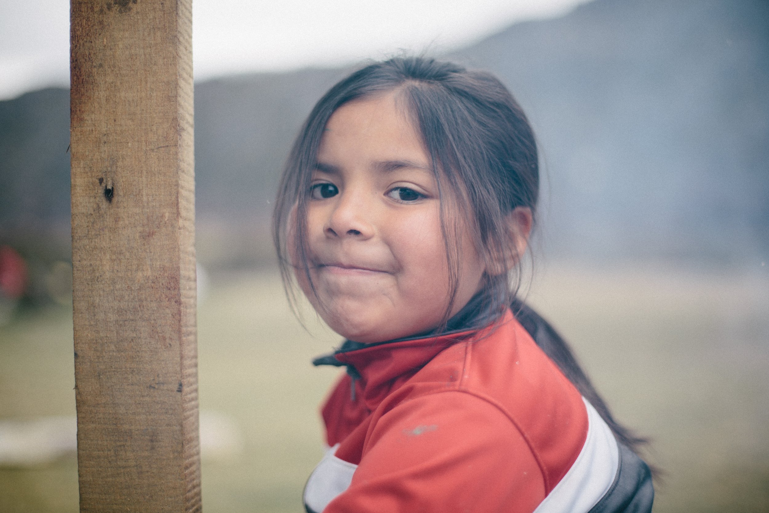 Niña con chaqueta roja al lado de un poste de madera al aire libre.
