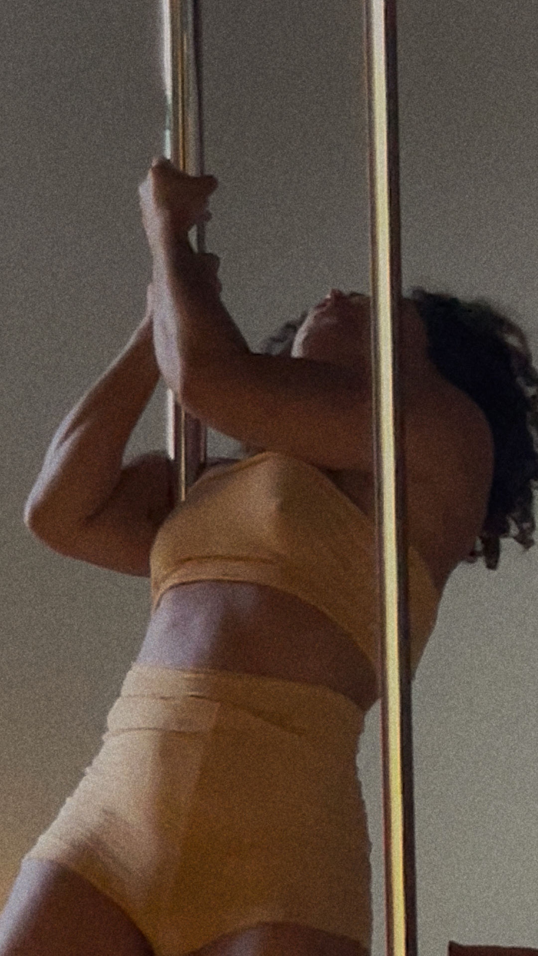 Woman holding the pole mid-session, biceps and abs engaged, reflected in the studio mirror