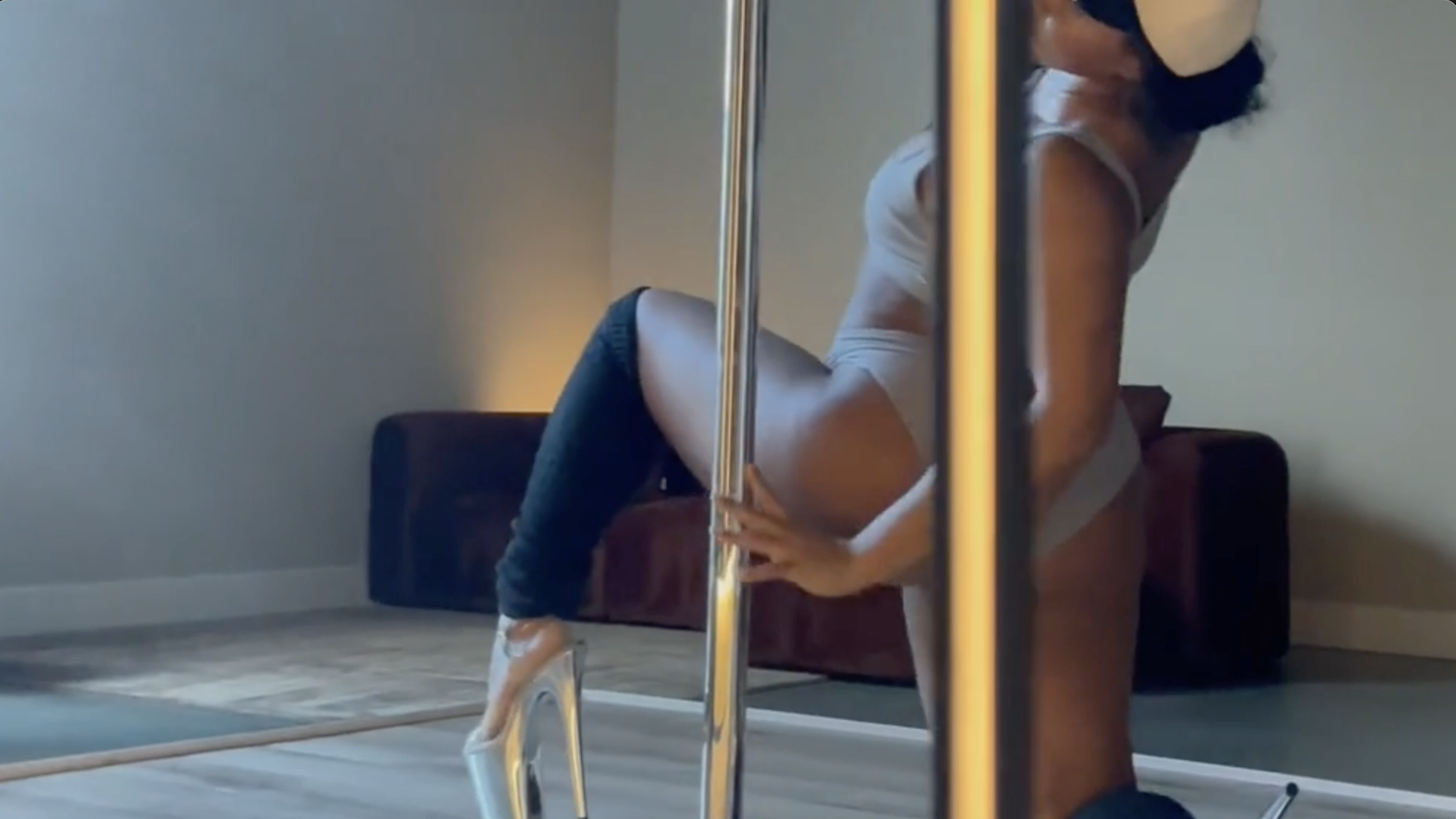 Woman in a lunge at the chrome pole wearing chrome platform heels, reflected in the mirror — PoleBait Haus pole dance heels training in Los Angeles