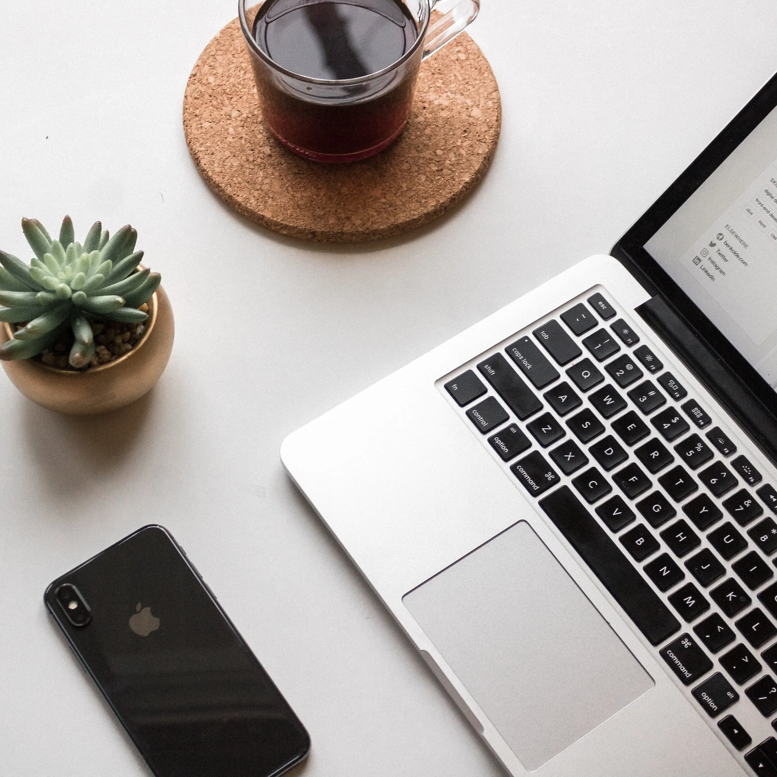 health and wellness copywriter's desk.  Laptop, plant, phone and coffee on grey desk.
