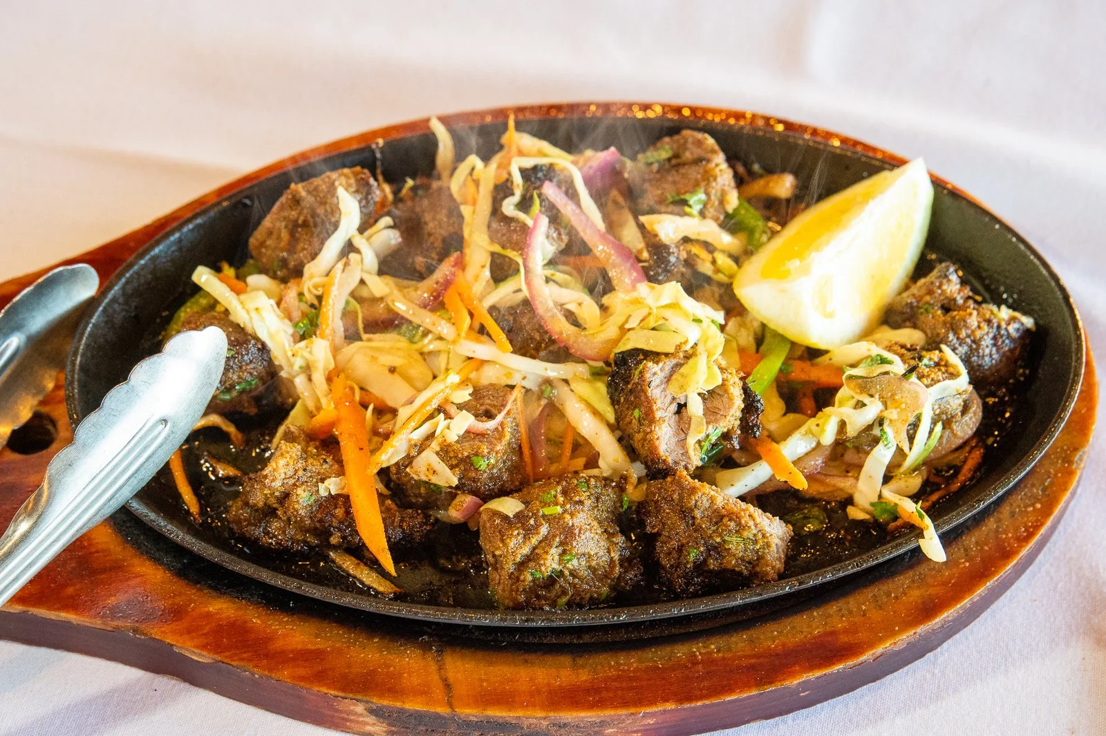 Mexican sizzling beef fajitas with grilled beef chunks, sautéed vegetables, and a lemon wedge on a cast iron skillet.