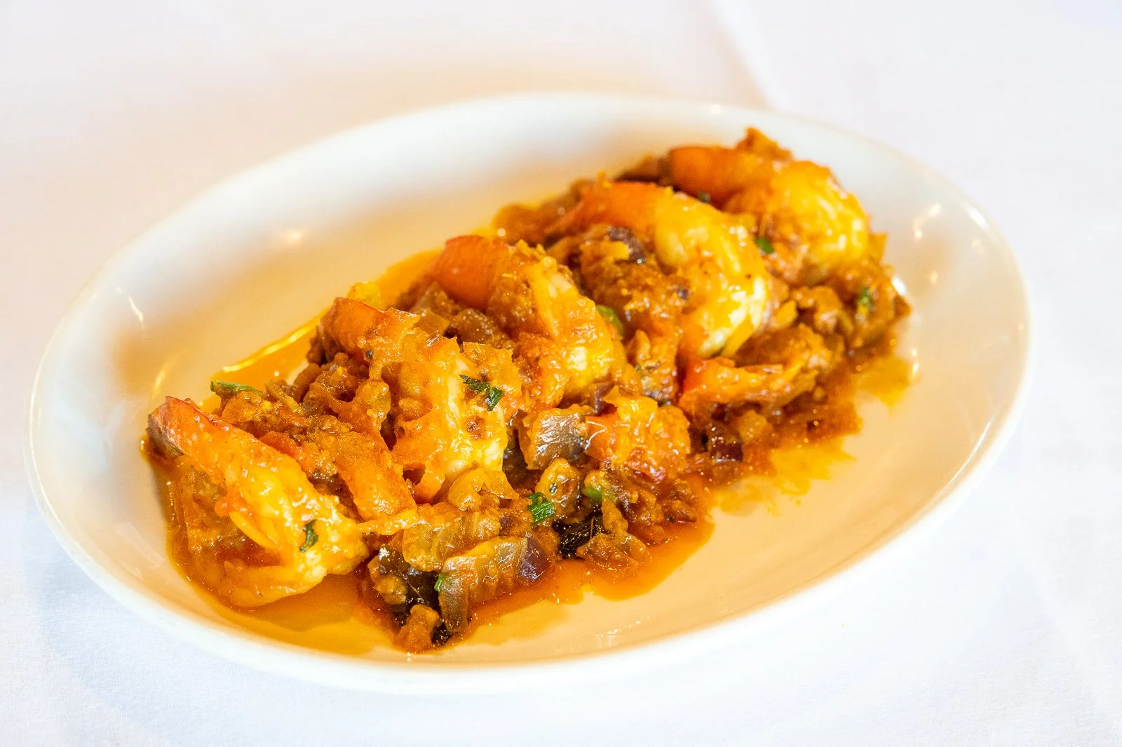 A white dish of spicy scrambled eggs with vegetables and sauce, garnished with chopped herbs on a white tablecloth.