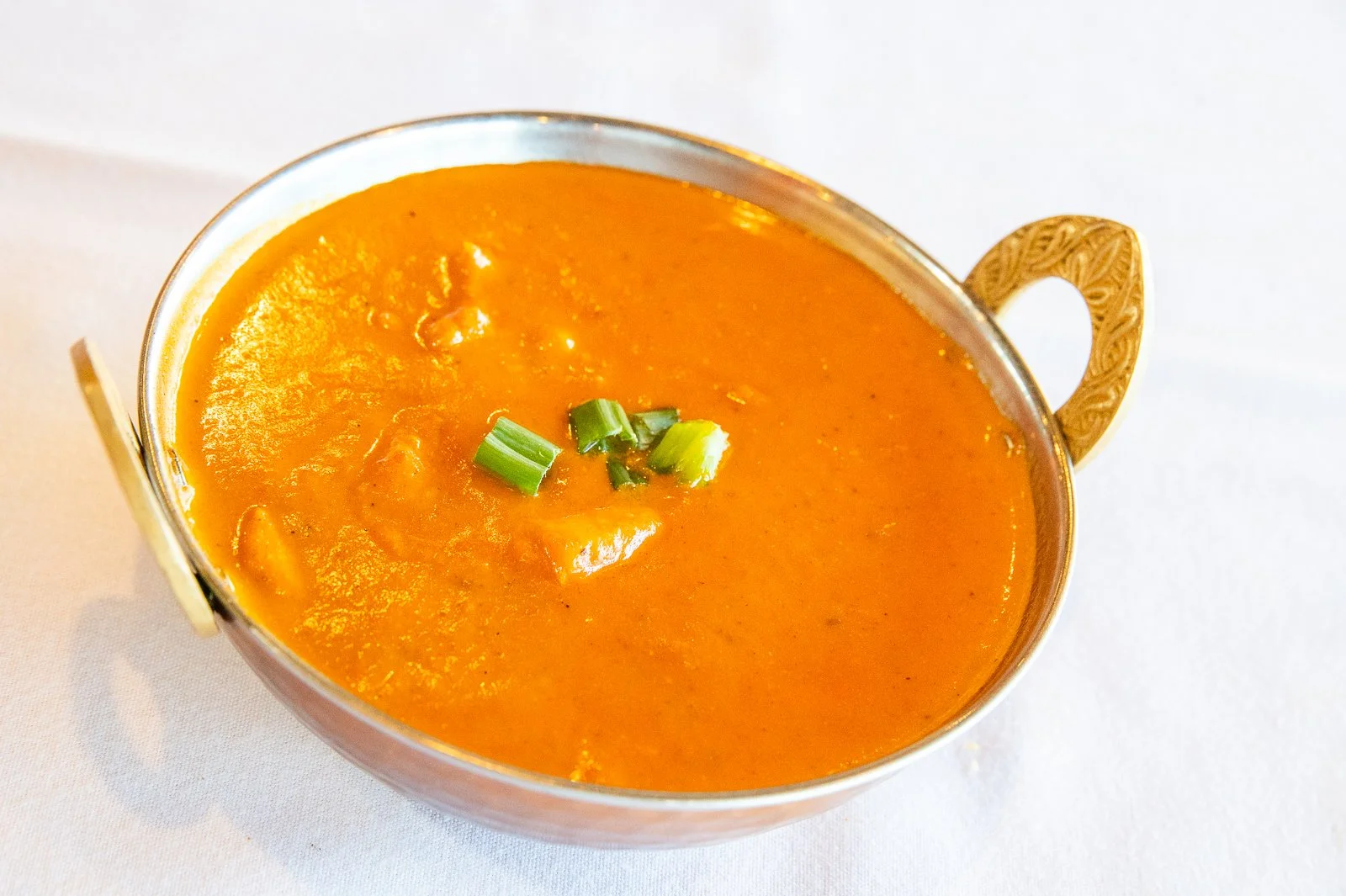 A bowl of orange-colored soup garnished with chopped green onions.
