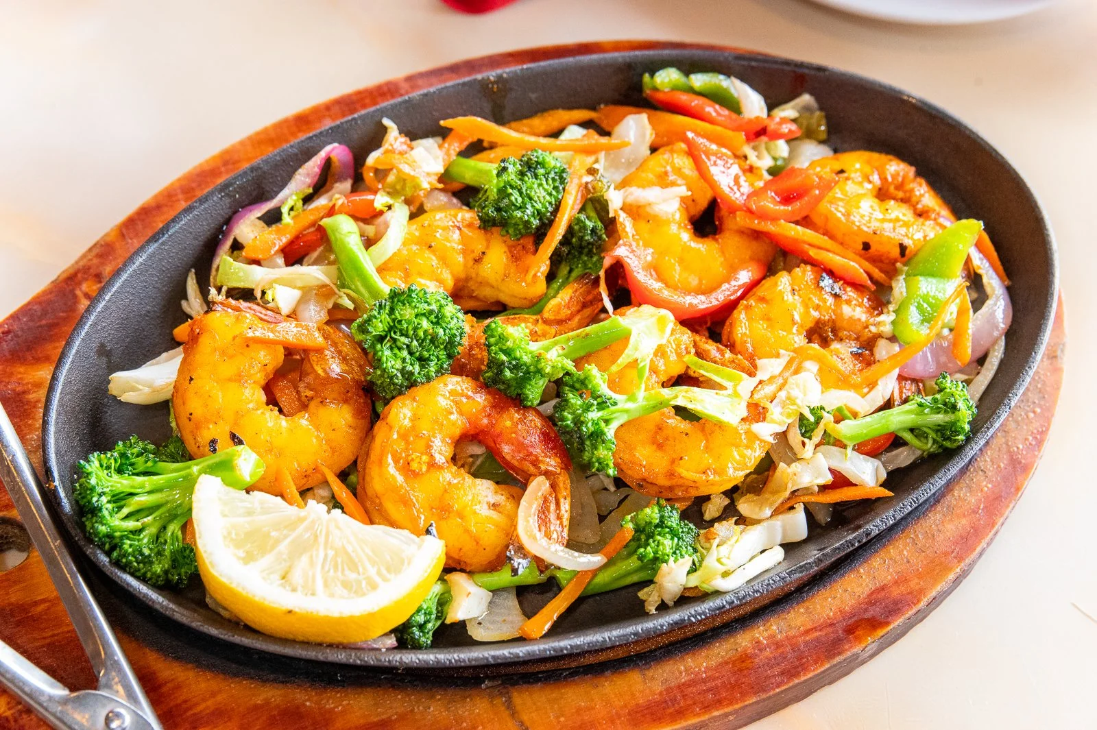Shrimp and vegetable stir-fry with broccoli, bell peppers, carrots, cabbage, and lemon wedge on a sizzling hot plate.