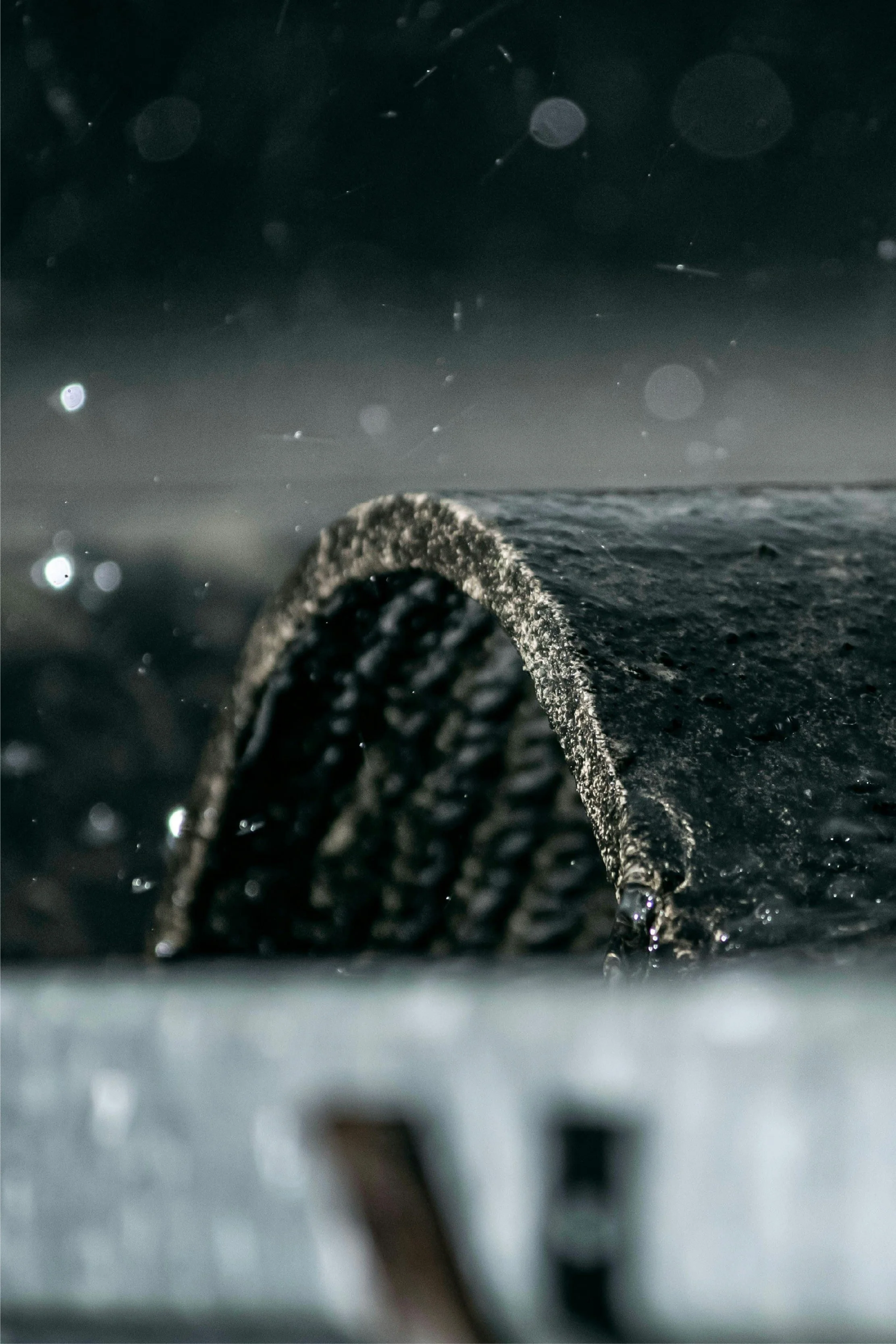 Une pièce de pneu de voiture vue de près sur une surface noire humide, avec un fond flou et sombre.
