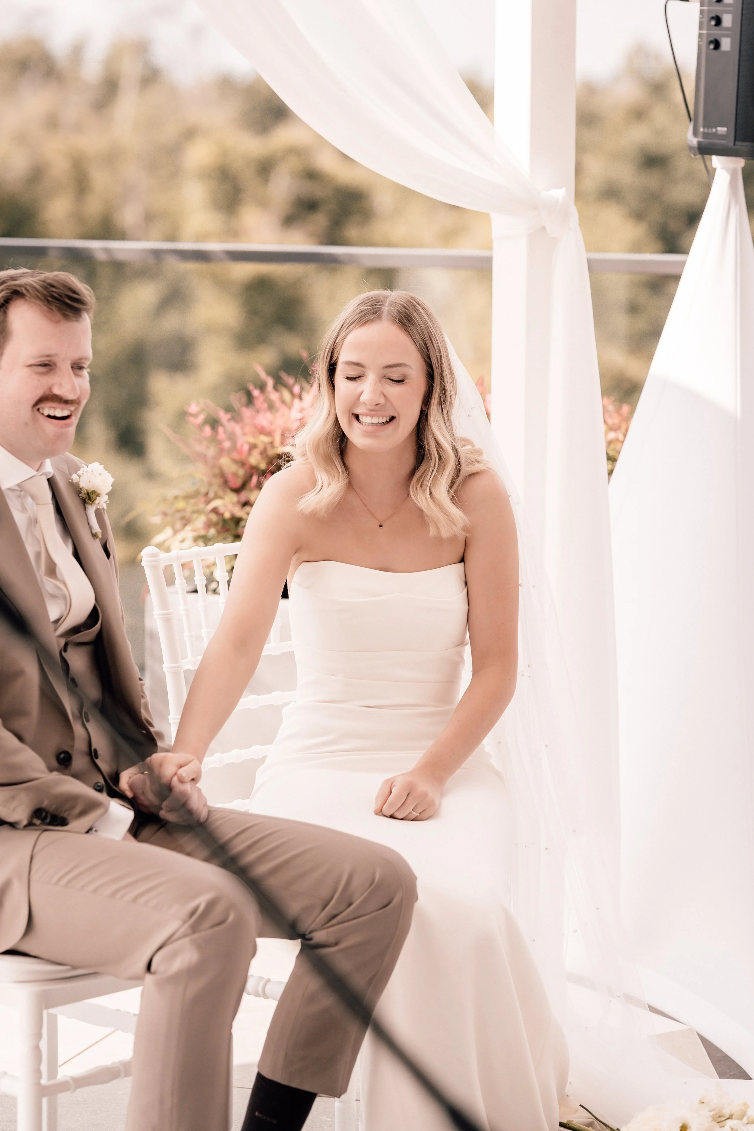 Braut und Bräutigam bei ihrer Hochzeit, lachend und Händchen haltend, in einer weißen Hochzeitsausstattung. Sven Goos Fotografie