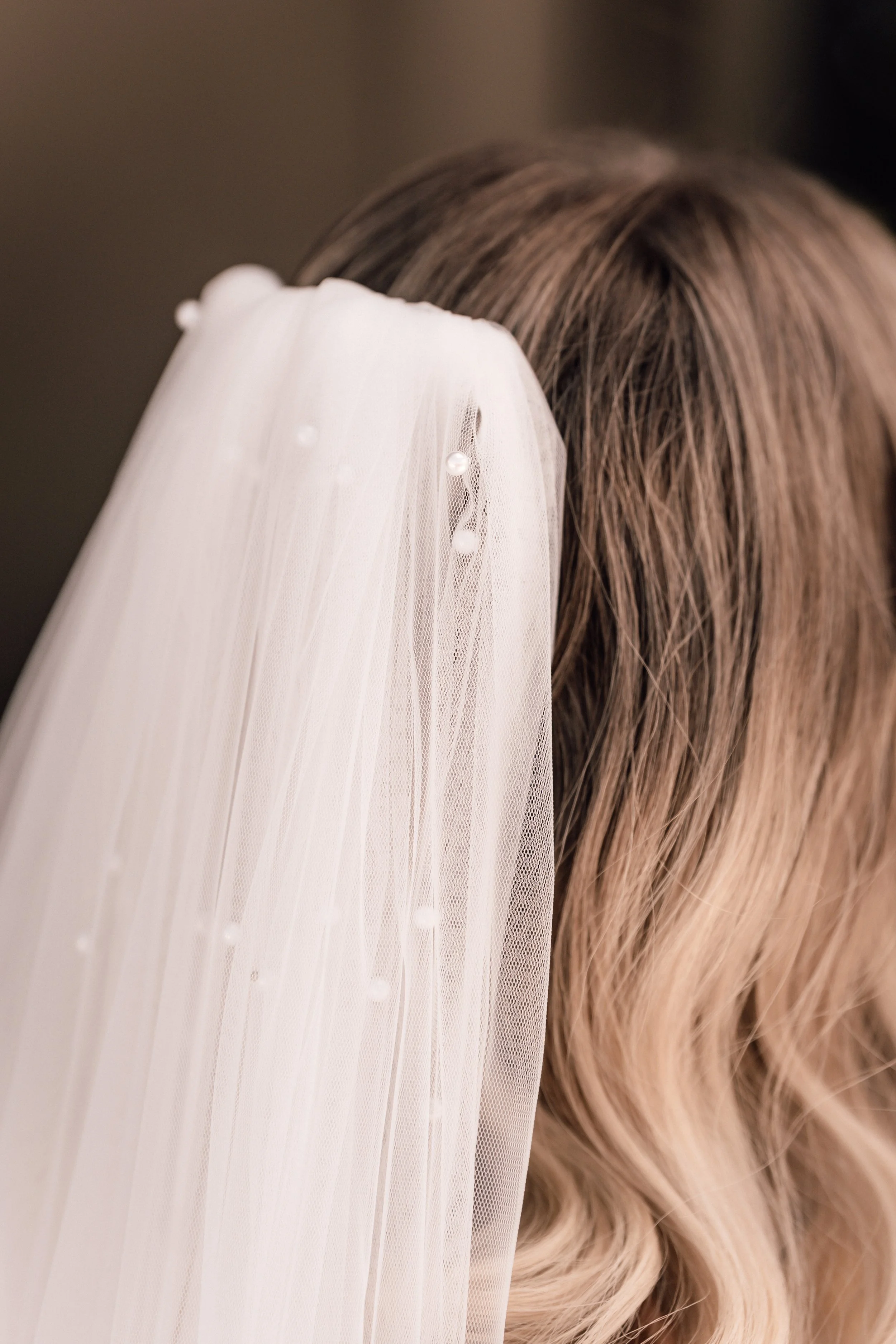 Nahaufnahme eines weißen Hochzeitsfederkranzes mit Perlen, der an einem braunen, gewellten Haar befestigt ist. Sven Goos Fotografie