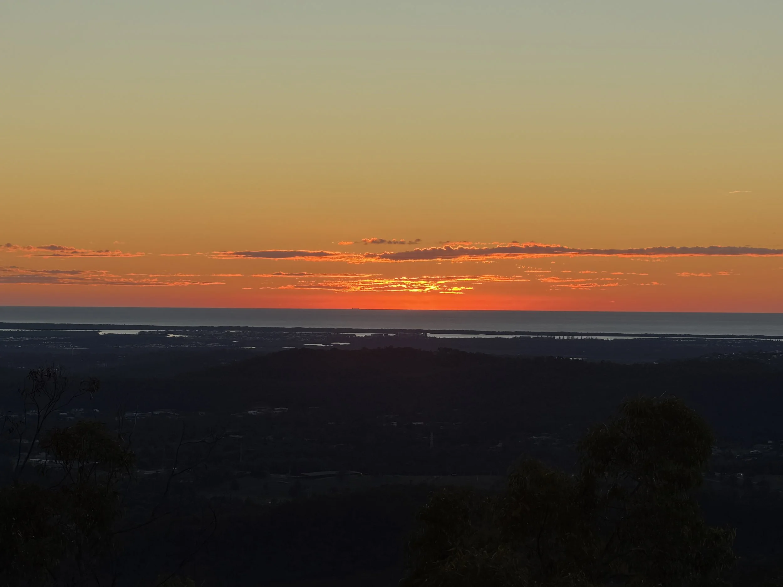 Sunset over a body of water with a dark silhouette of land and trees in the foreground.