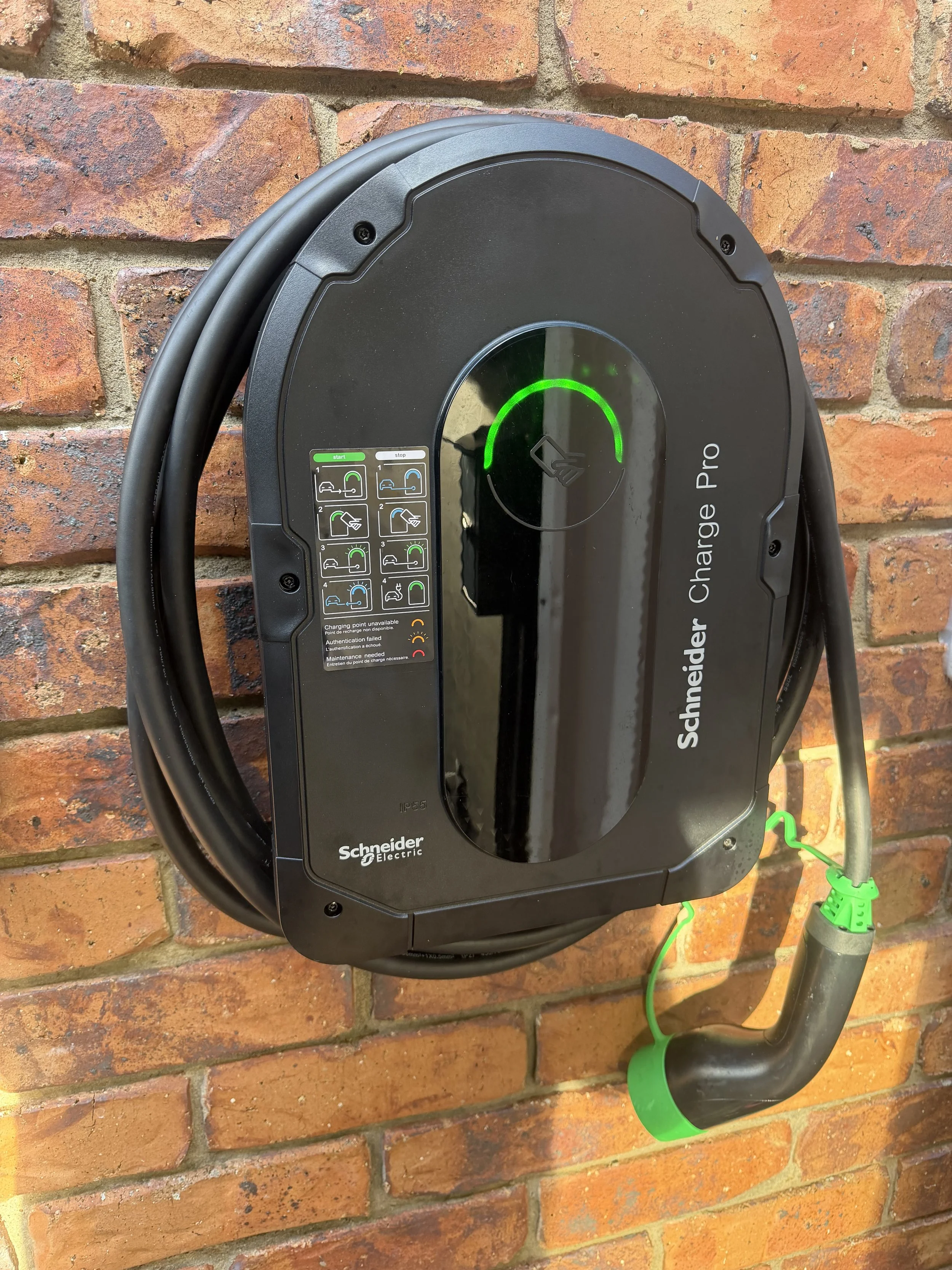 Schneider Electric electric vehicle charger mounted on a brick wall with green indicator light on