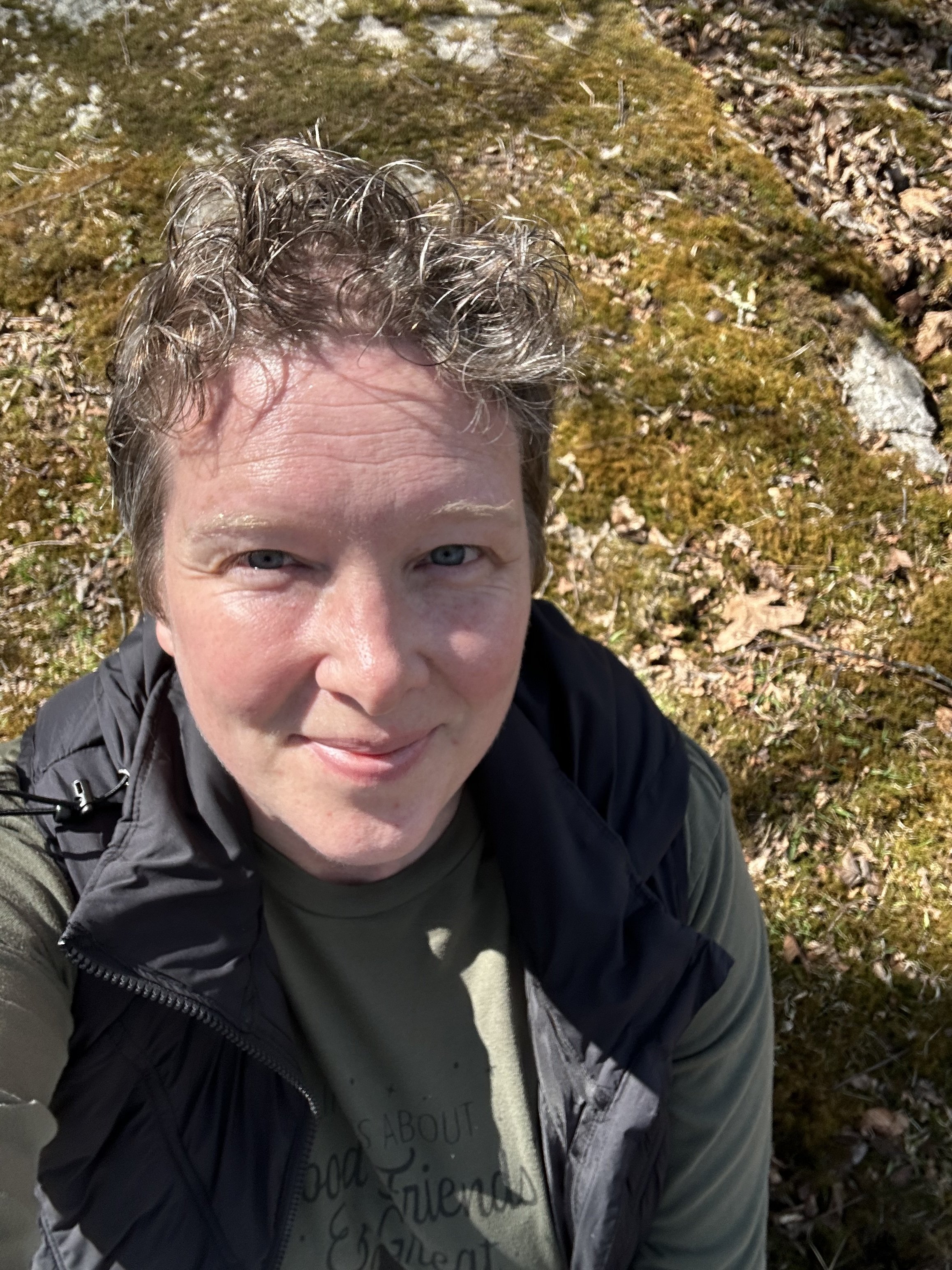 Woman sitting on a moss-covered rock in the sun.