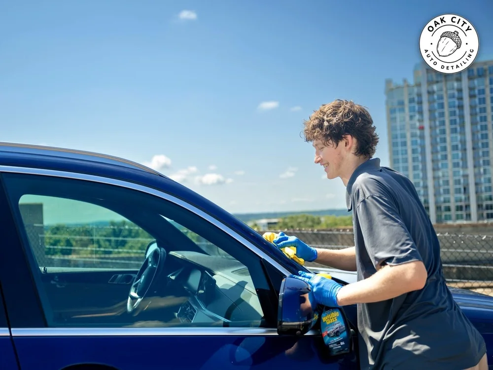 Oak City technician in uniform detailing a BMW with downtown Raleigh behind him