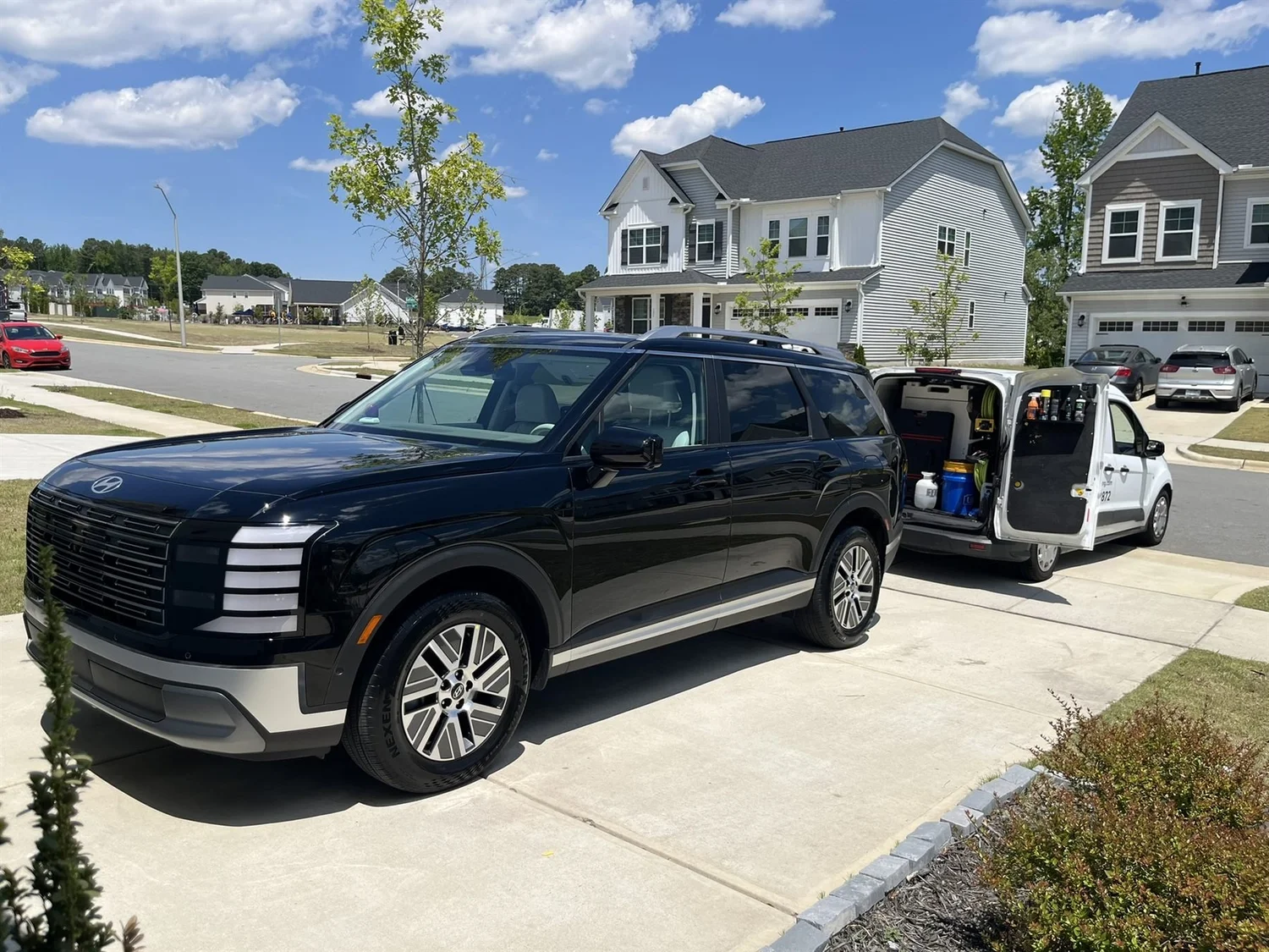 Freshly detailed black SUV in a Triangle driveway with the Oak City mobile detailing van