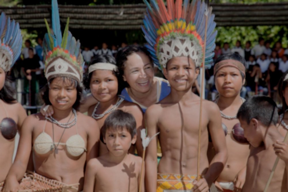 Ruth Consuelo Chaparro, directora de FUCAI, junto a niñas, niños y jóvenes indígenas con tocados de plumas