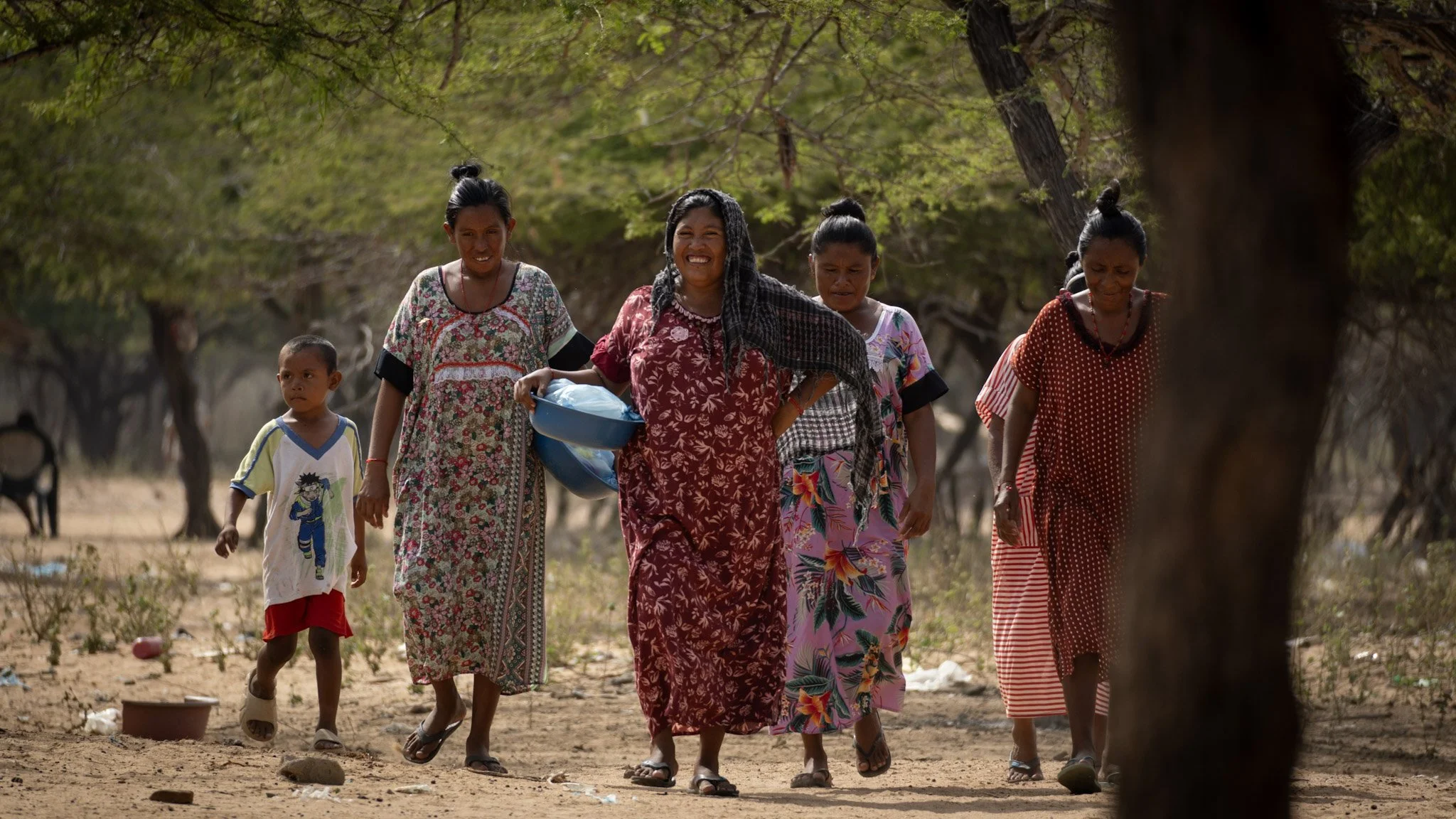 Grupo de mujeres y un niño caminando por un camino de tierra en un entorno natural con árboles verdes.
