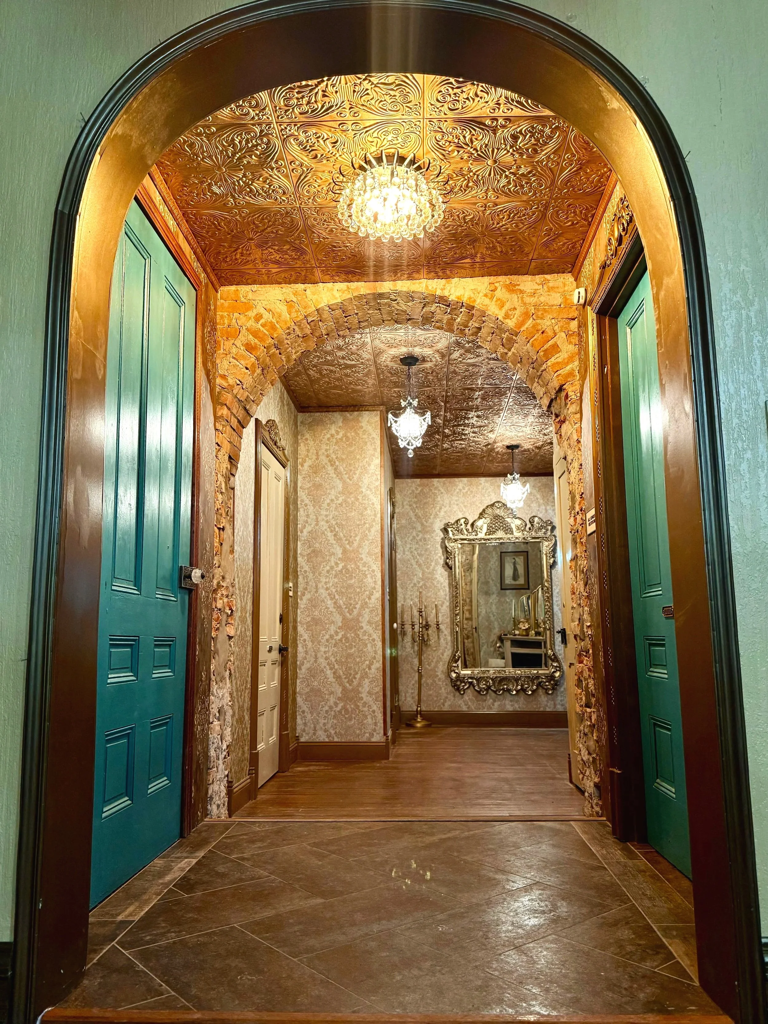 Archway leading to the bathrooms in the hallway of The Relic with beautiful chandeliers and large mirror.