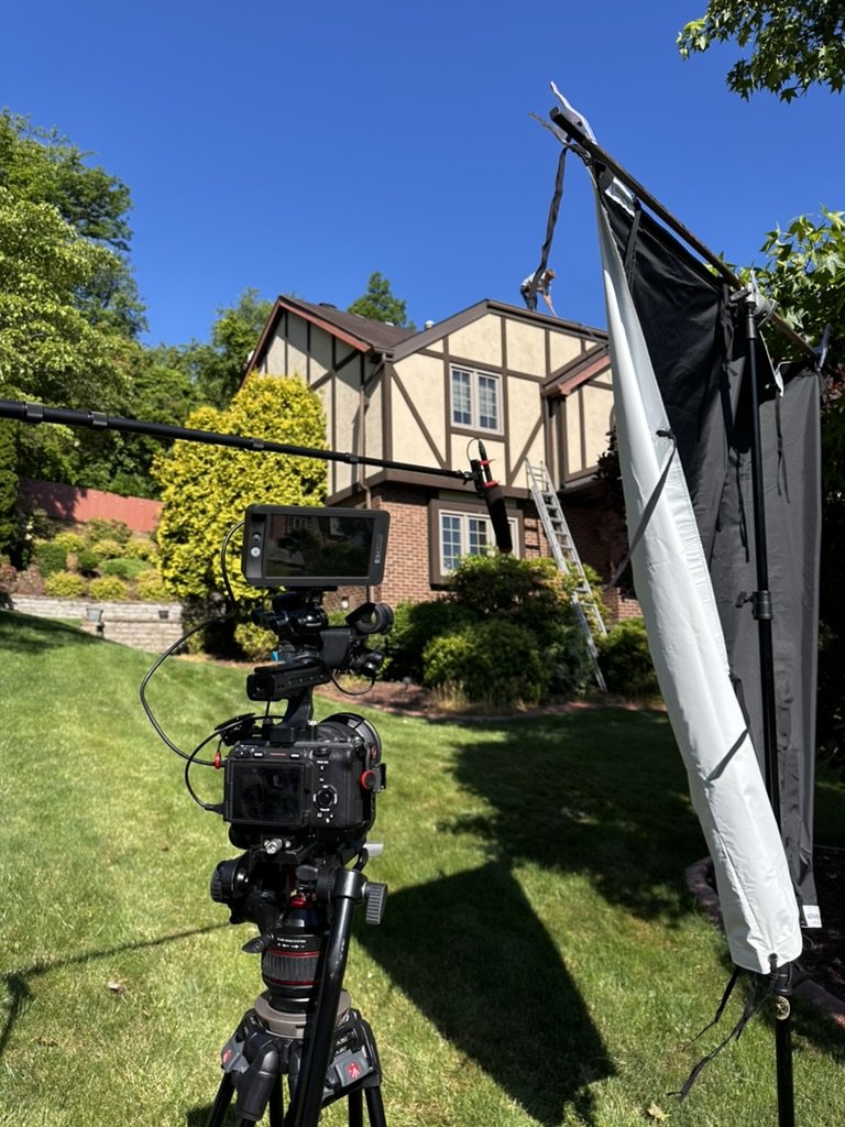 Filmmaking setup in front of a suburban house with camera and lighting equipment on lawn