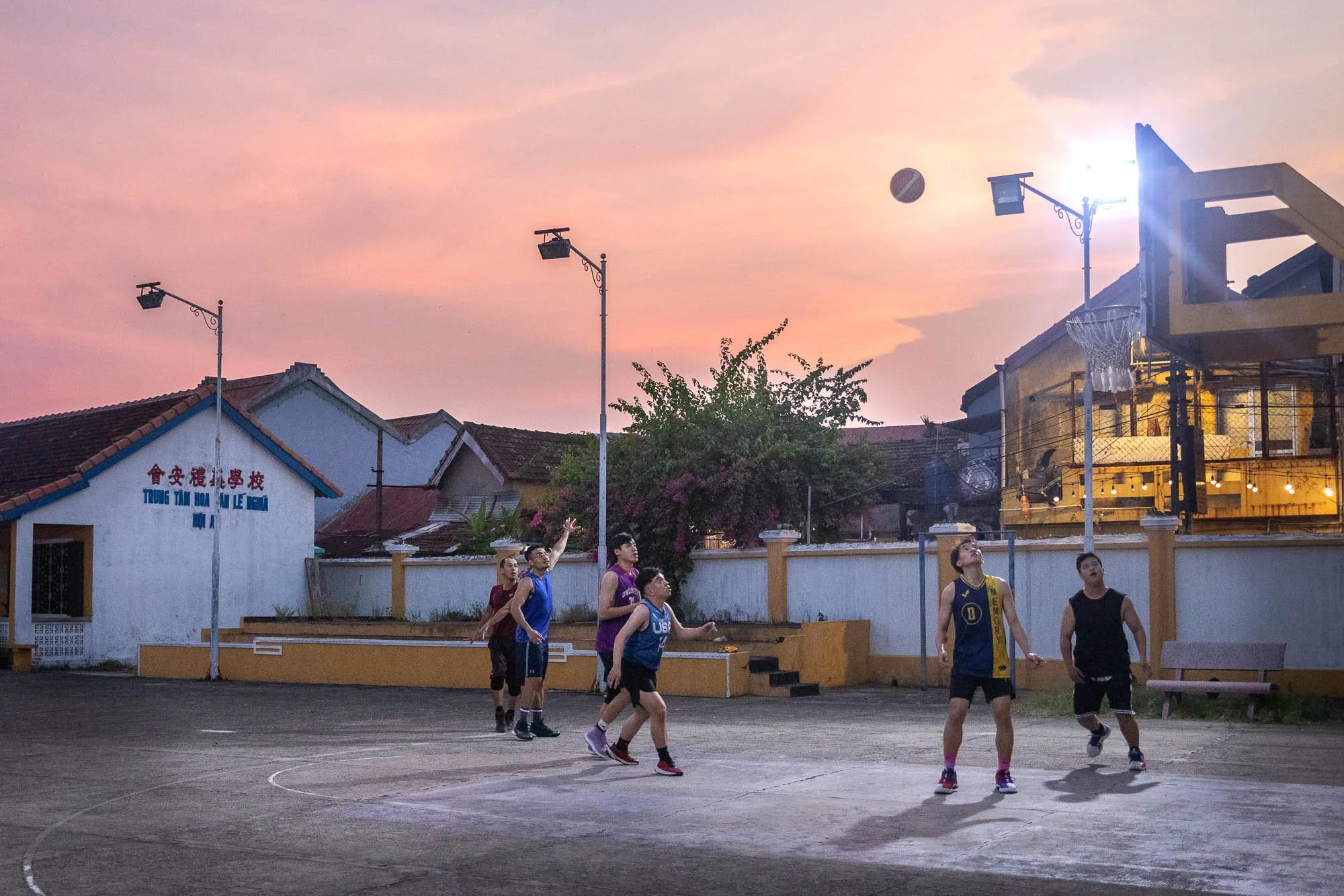 Youth playing basketball on an outdoor court at sunset in Vietnam