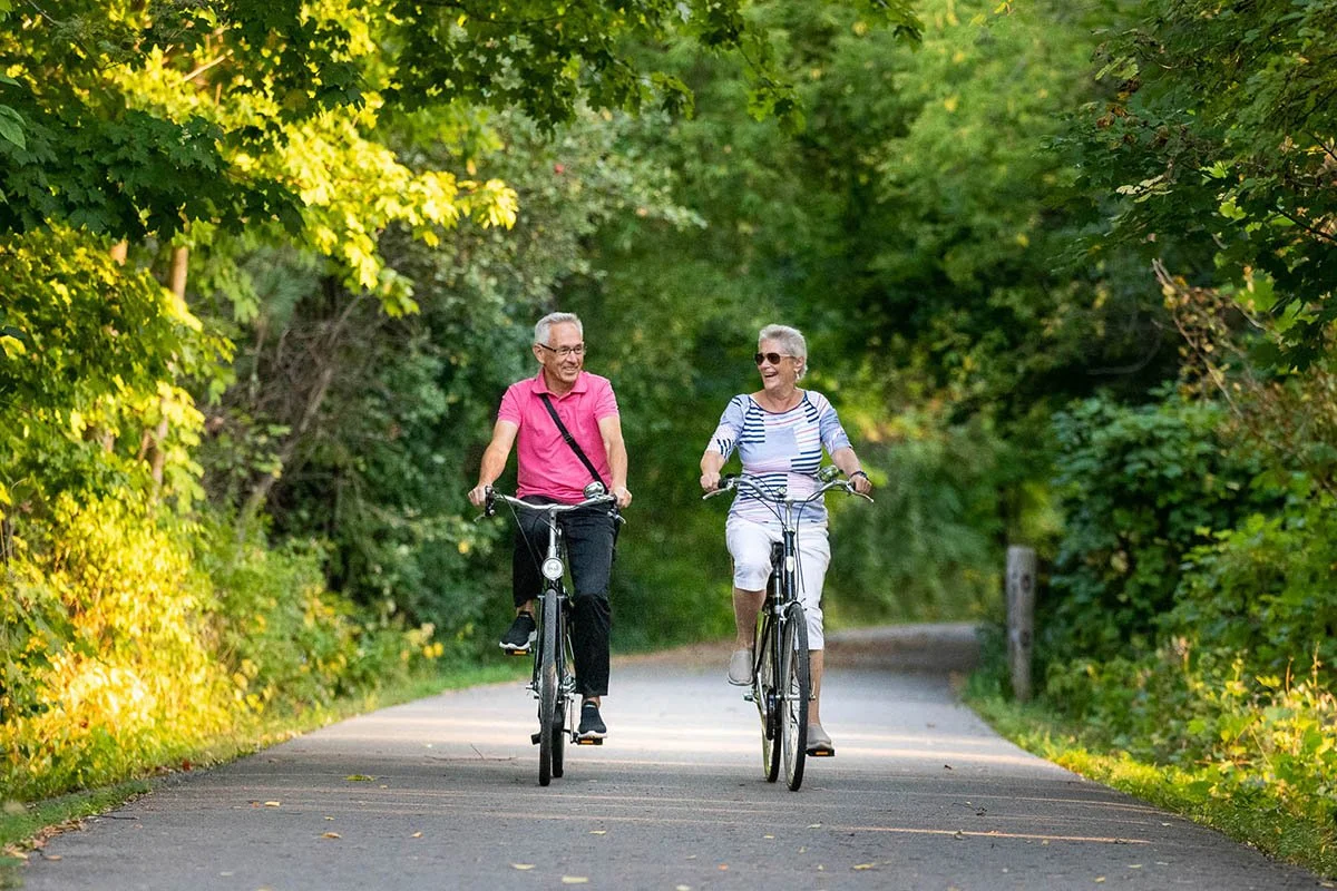 a senior couple laughing ride bicycles on a wooded trail