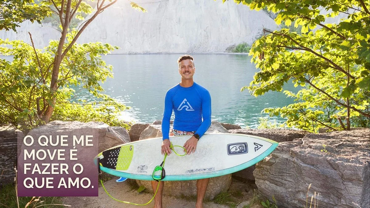 a male poses for a portrait with his surfboard in front of calm waters