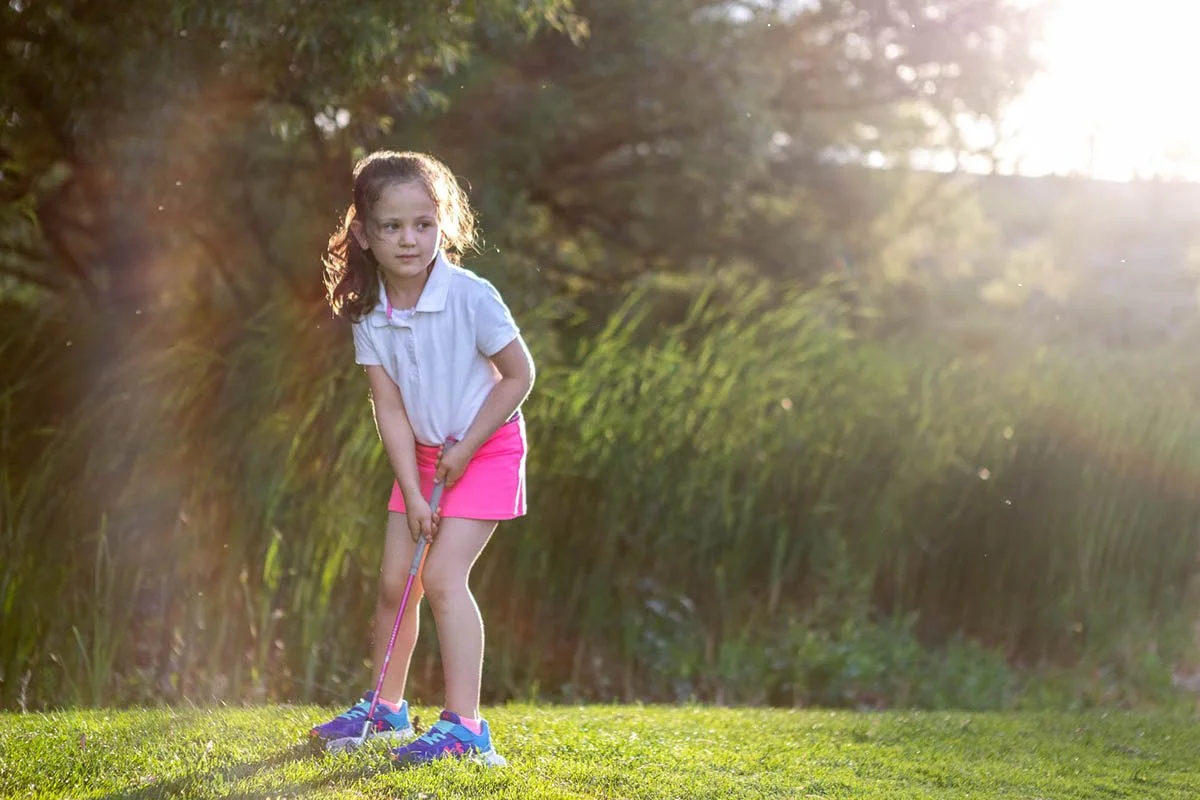 Emma pratica sua tacada ao ar livre em um campo de golfe.