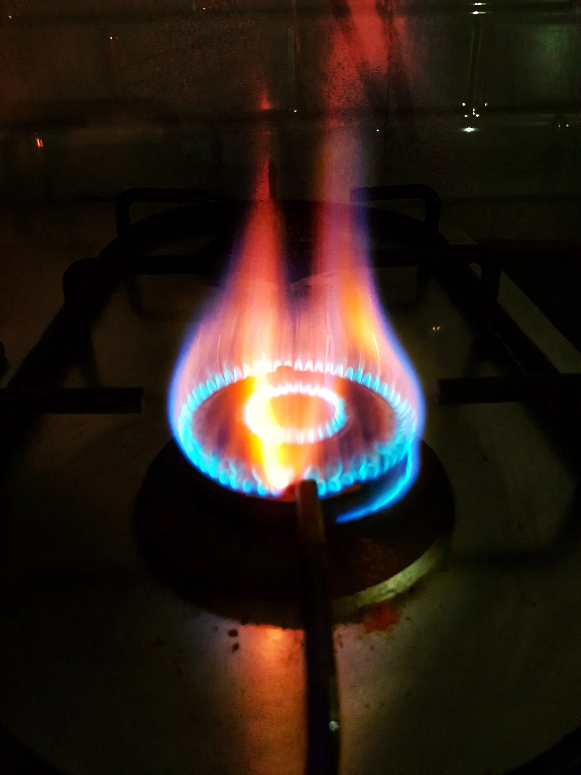 Close-up of a blue and orange gas flame on a stovetop burner.
