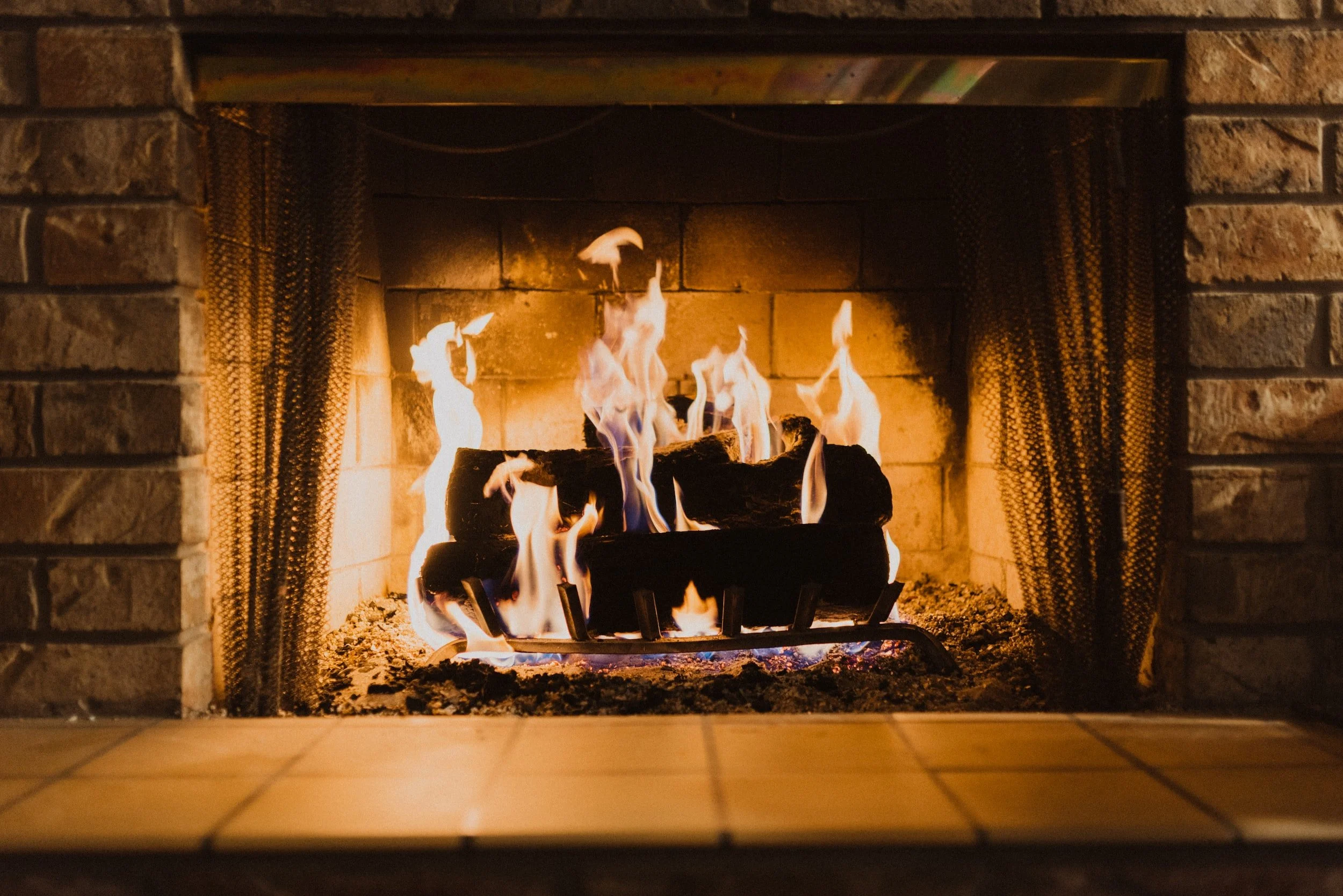 A cozy fireplace with burning logs and flames in a brick hearth.