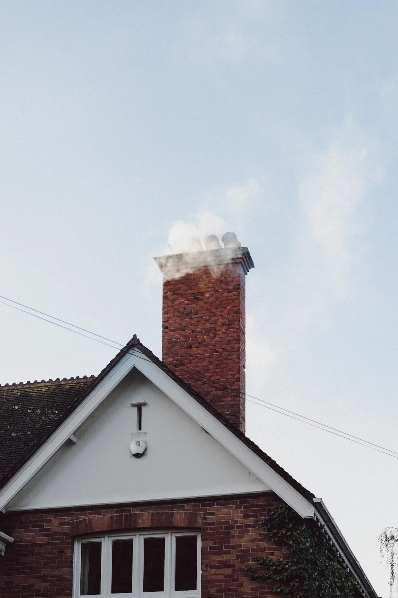 A house with a brick chimney emitting smoke on a cloudy day.