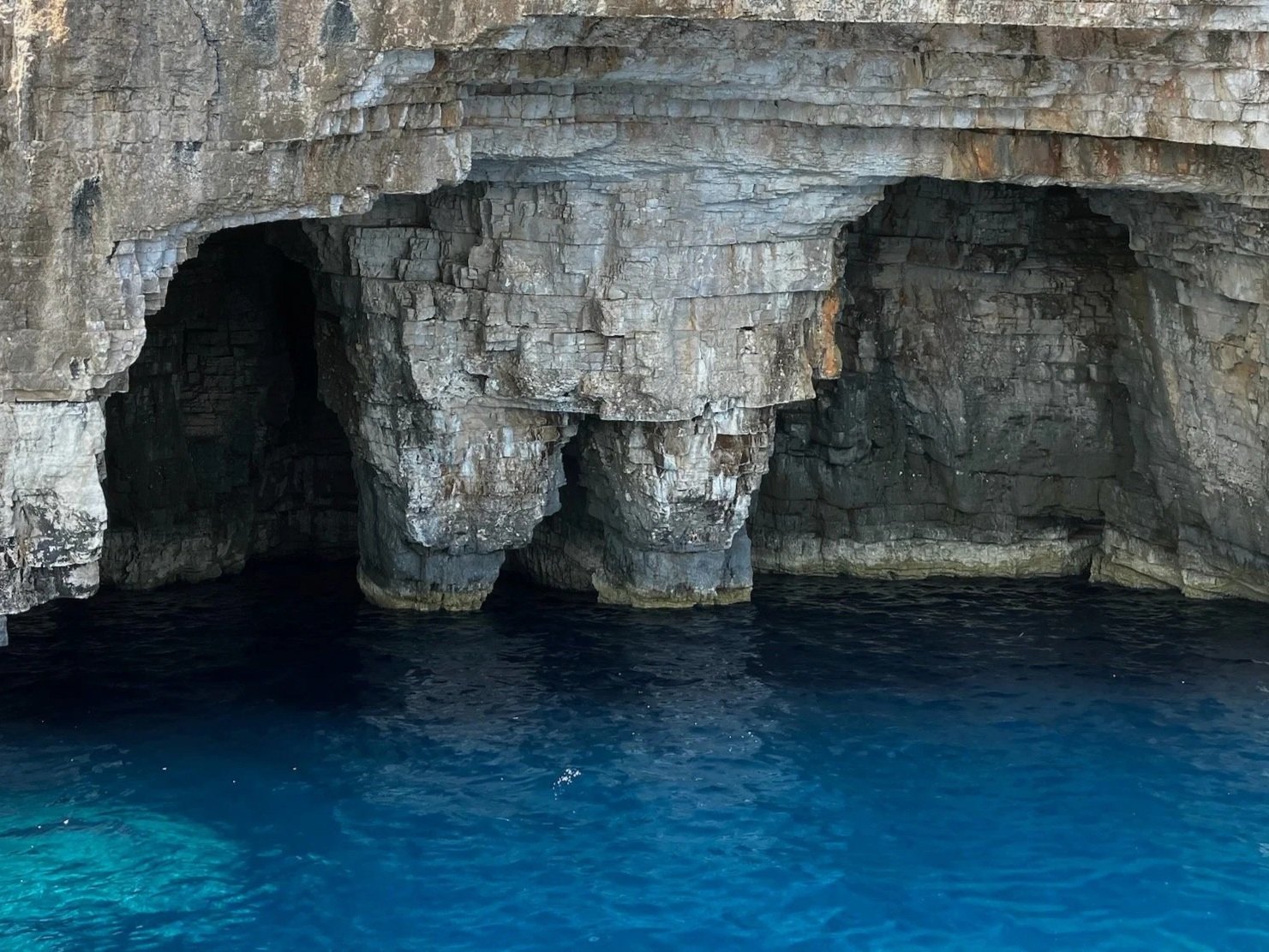 Rock formations with caves rising above deep blue water.