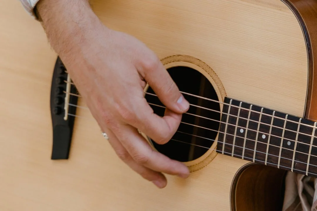 Close-up of a person's hand playing an acoustic guitar, pressing down on the strings near the sound hole.