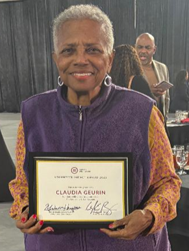 Image of an older african american femail holding a recognation document wearing a purple jacket.