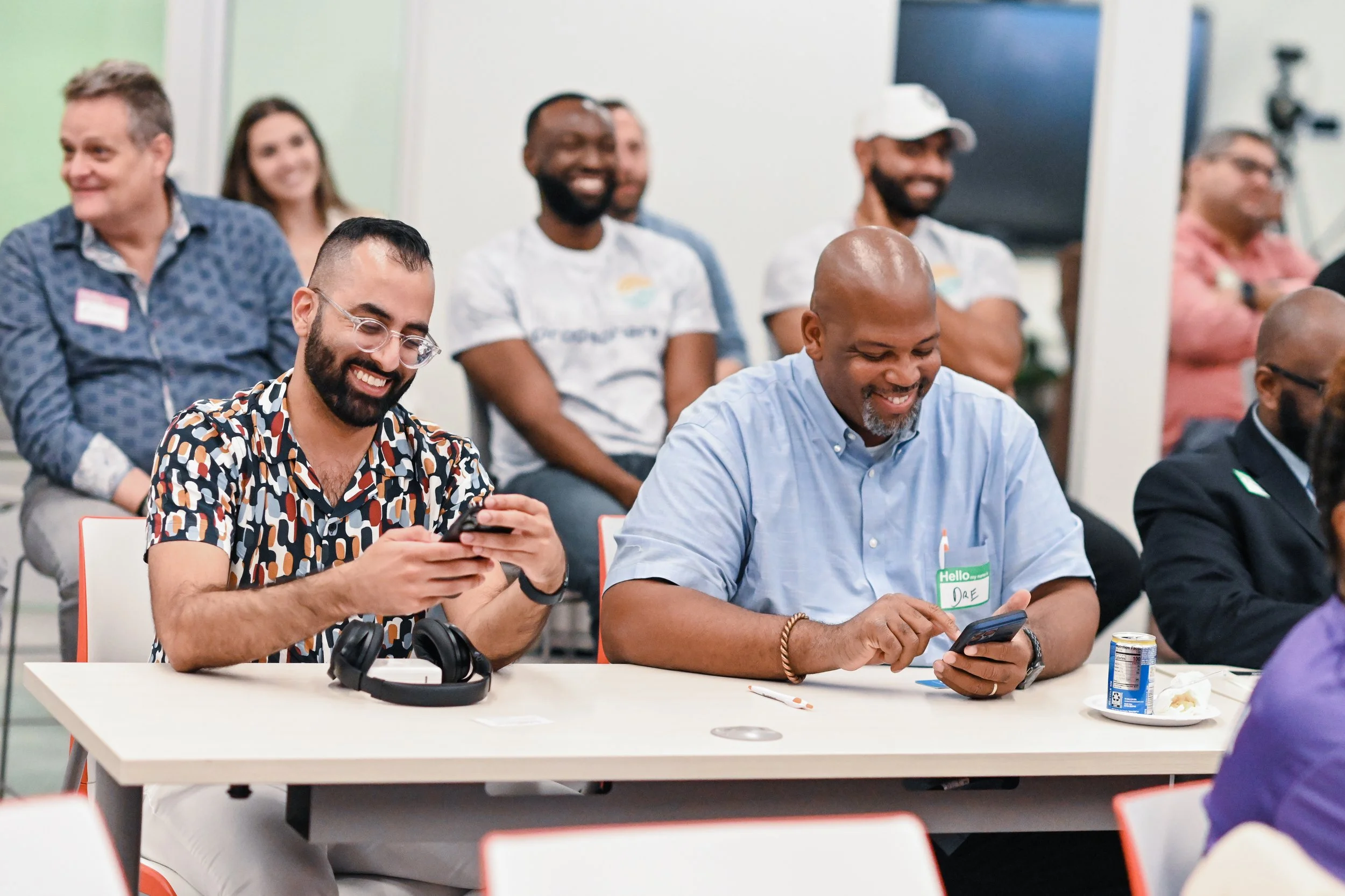 Group of people sitting and standing in a meeting room, smiling and looking at their phones.