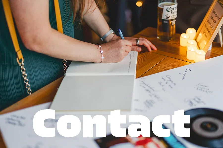 Person writing in a notebook at a wooden table with lit candles, a beer glass, and some papers around.