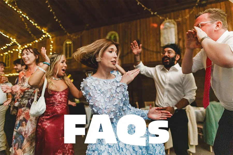People dancing and celebrating at a party or wedding reception in a rustic venue decorated with string lights.