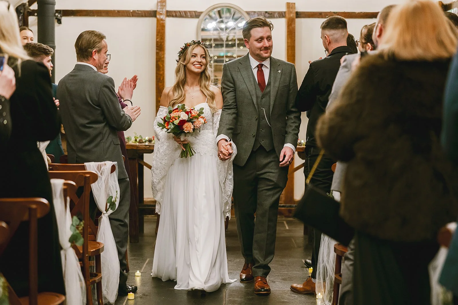 Bride and groom holding hands walking down the aisle during their wedding ceremony, surrounded by seated guests.
