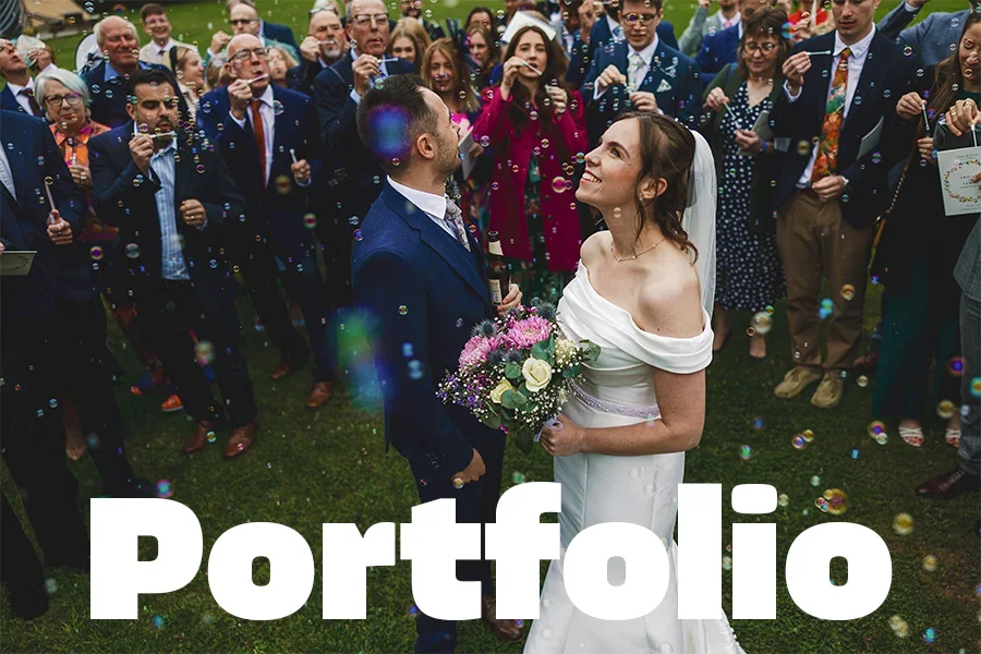 A bride and groom standing face to face at their wedding ceremony outdoors, surrounded by friends and family, with bubbles floating in the air and the word 'Portfolio' displayed at the bottom.