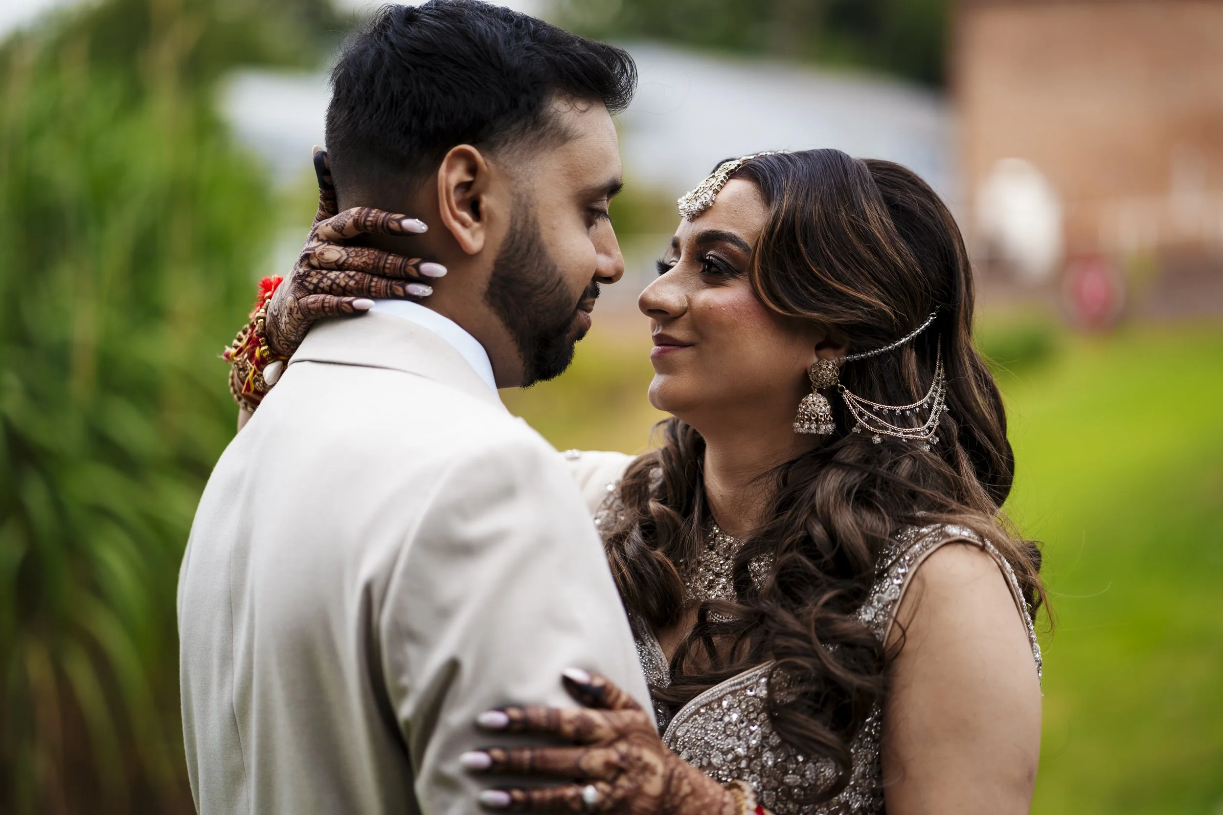 A couple in traditional Indian attire gazing into each other's eyes during a celebration outdoors.