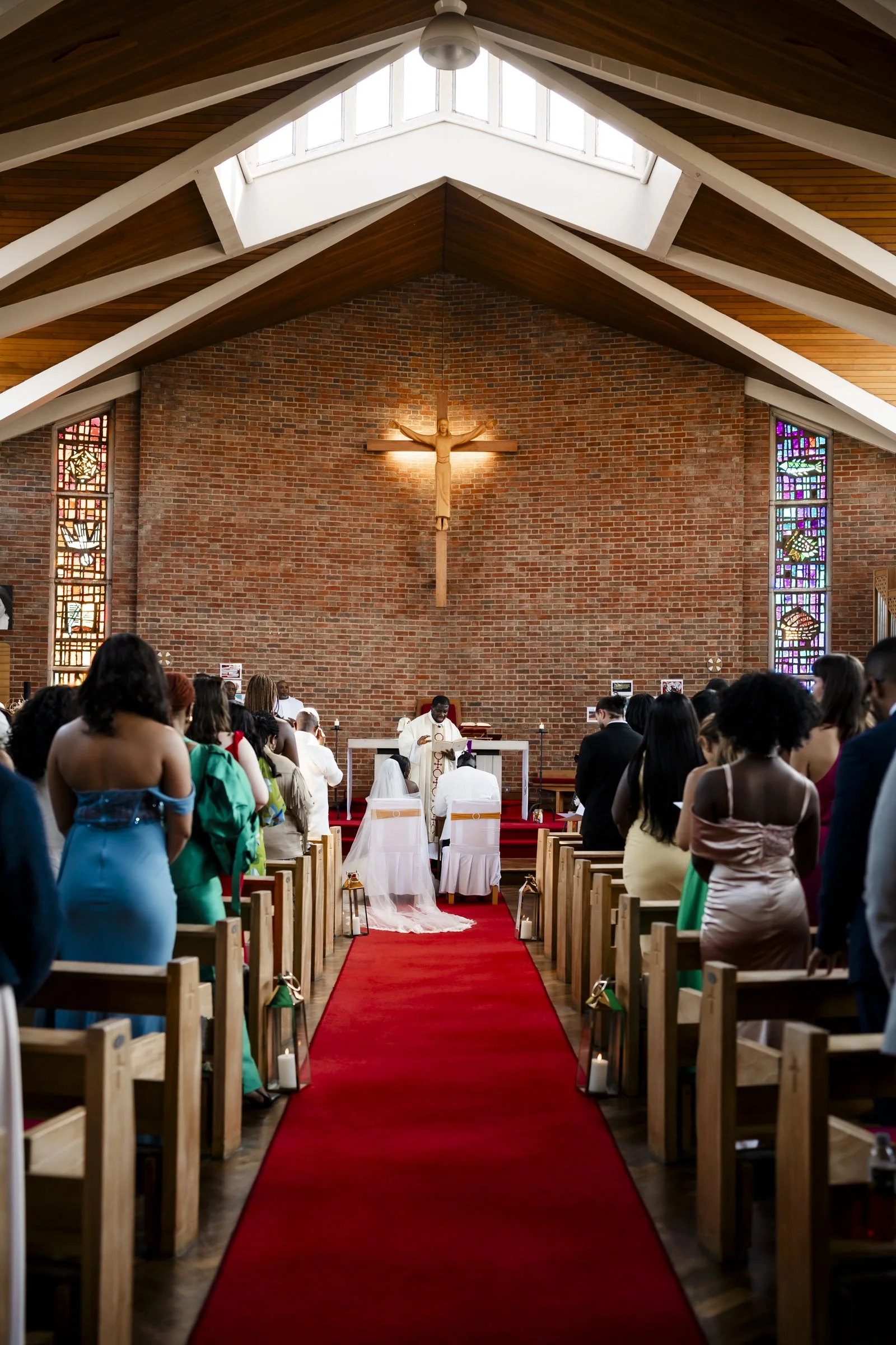Ghanaian church wedding ceremony with guests seated on either side of a red aisle. The officiant, dressed in white robes, stands at the altar. 
