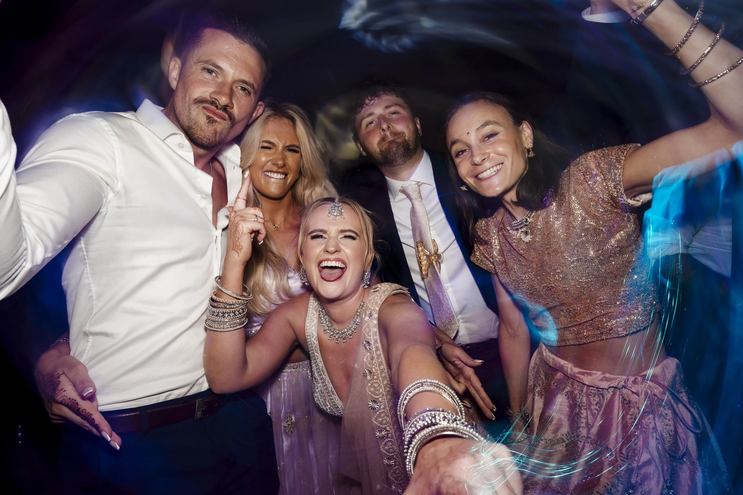Group of six diverse people celebrating and taking a selfie at a party, smiling and enjoying themselves, with colorful lighting.