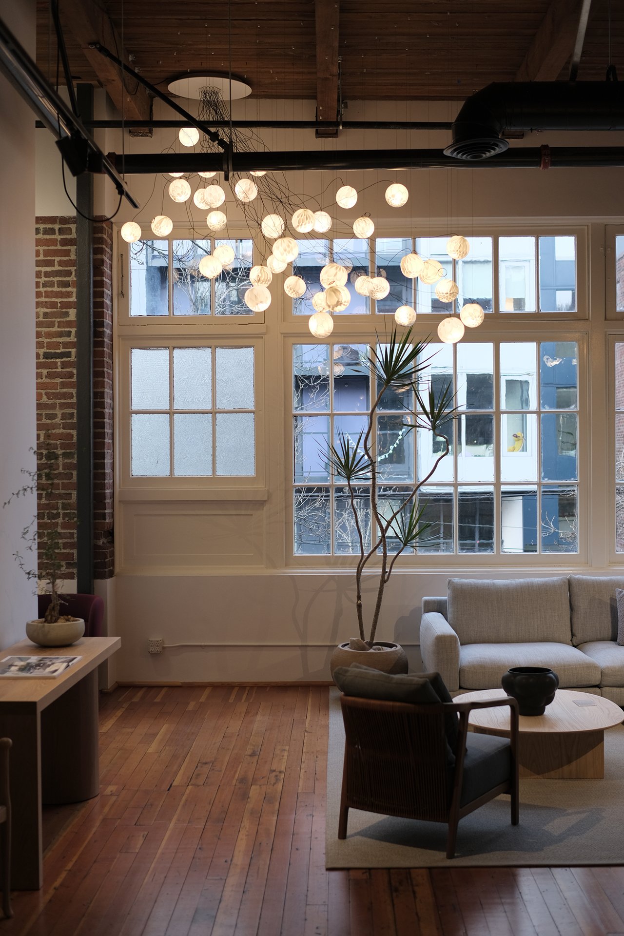Living room with large windows, hanging string lights, potted plant, beige sofa, and wooden furniture.
