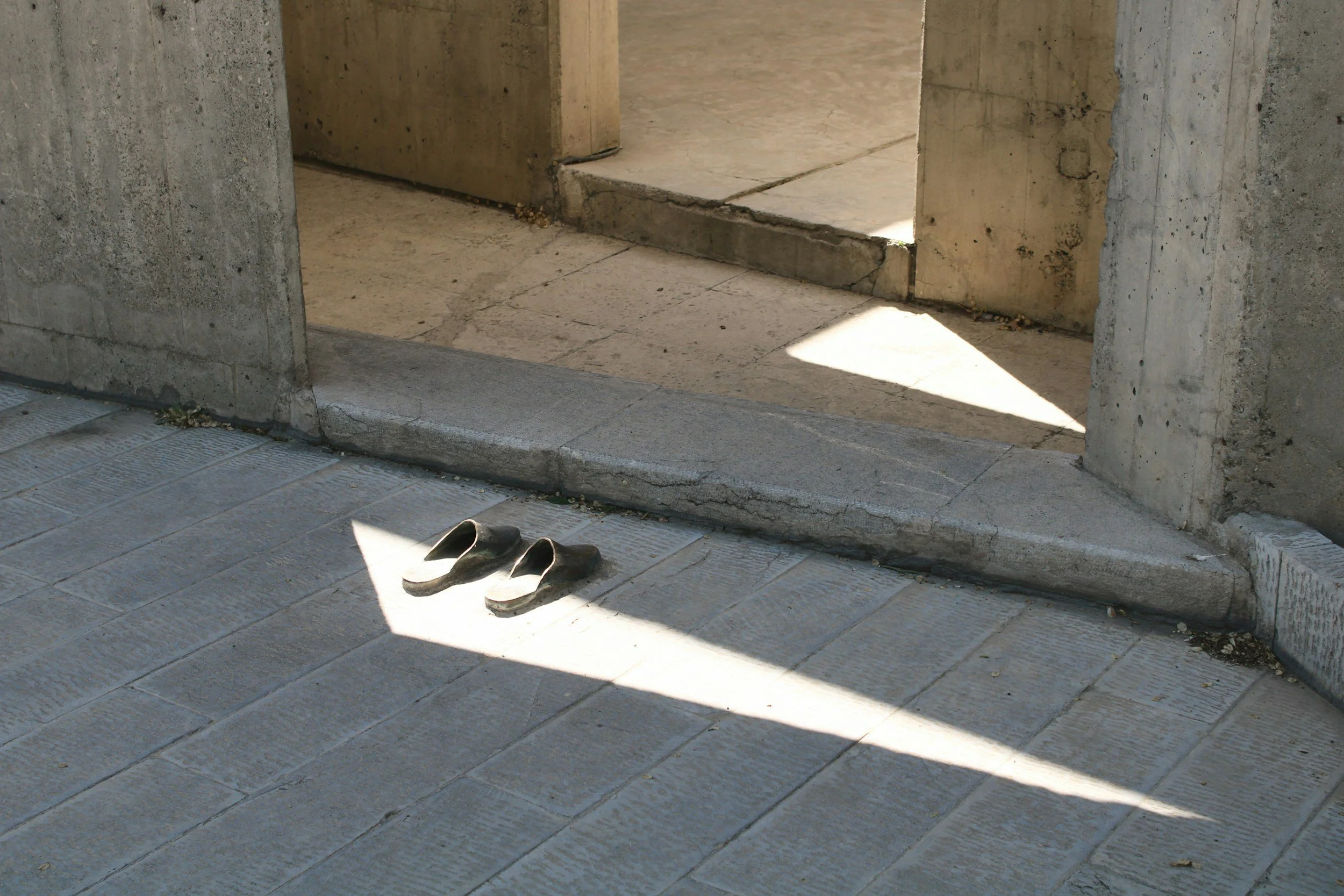 A pair of slip-on shoes resting in a shaft of natural light at a stone entryway