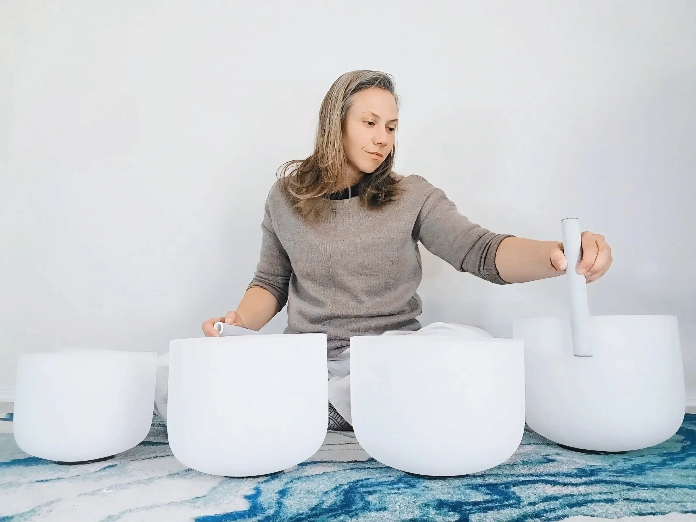 Erika Hood facilitating a sound bath with crystal singing bowls, creating a steady acoustic atmosphere for shared presence and quiet attention.