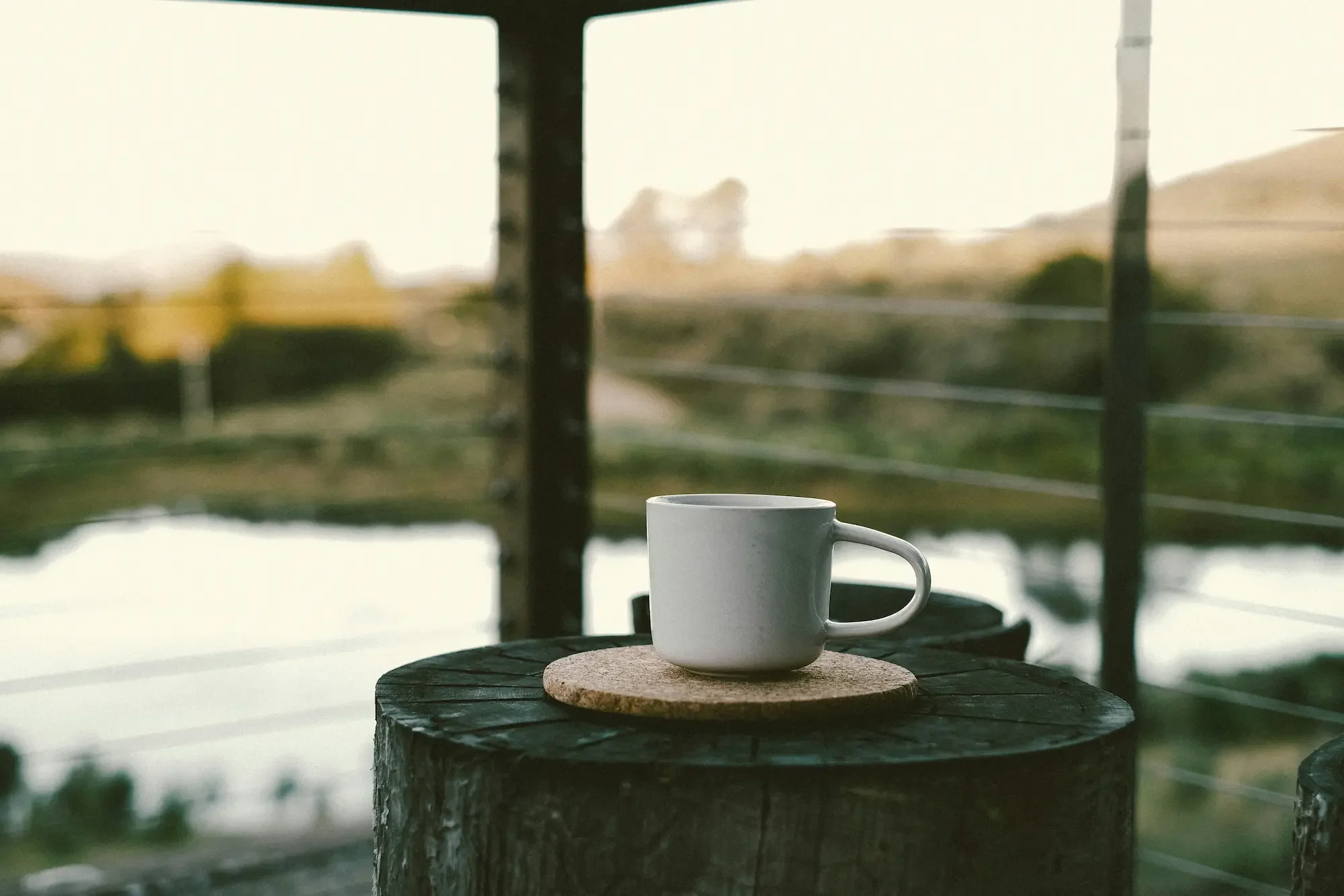 White ceramic coffee mug on a cork coaster resting on a log on an outdoor patio