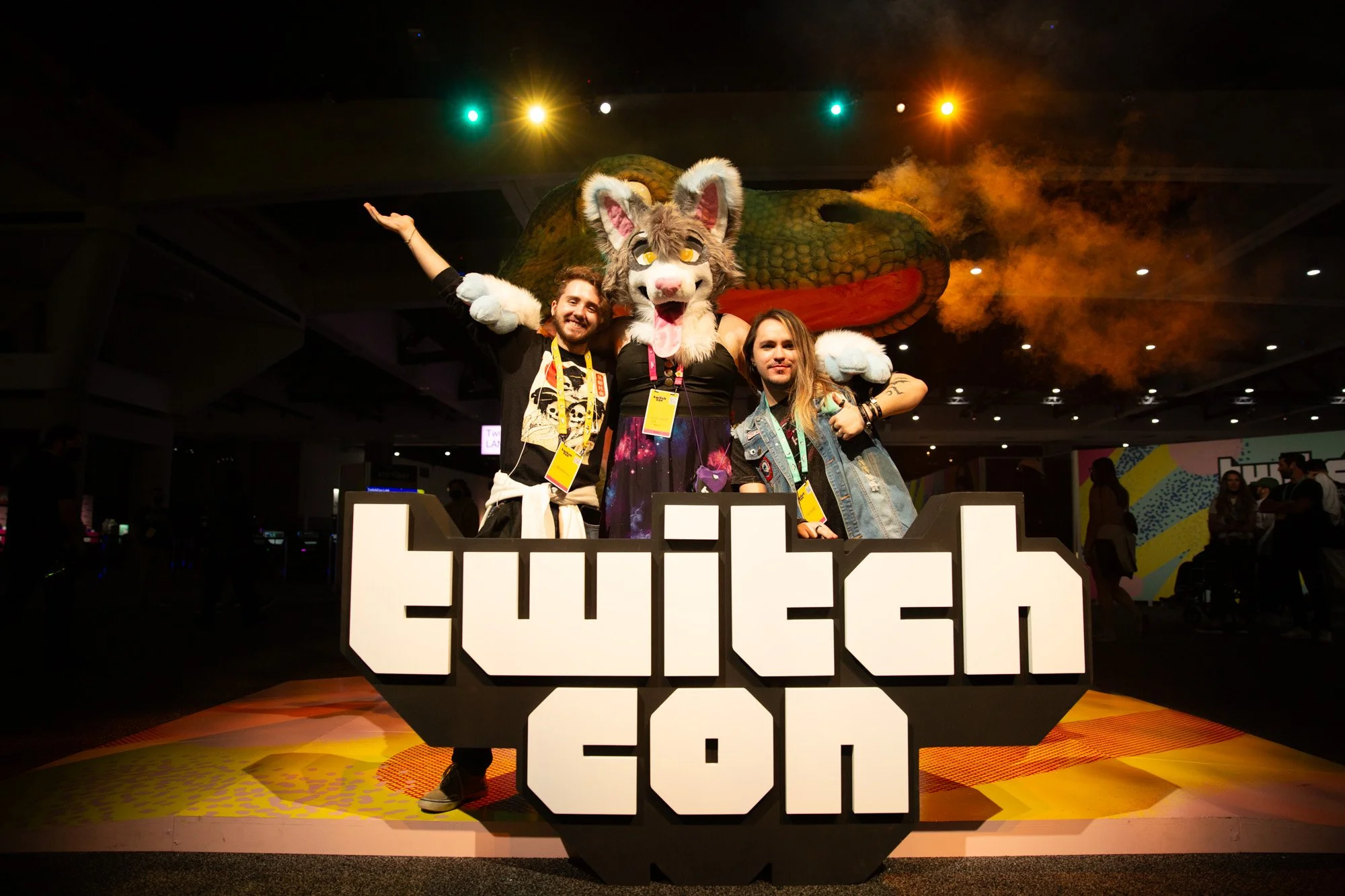 People posing with a person in a fursuit costume of a gray and white cat in front of a large dragon head prop on a stage at a convention.